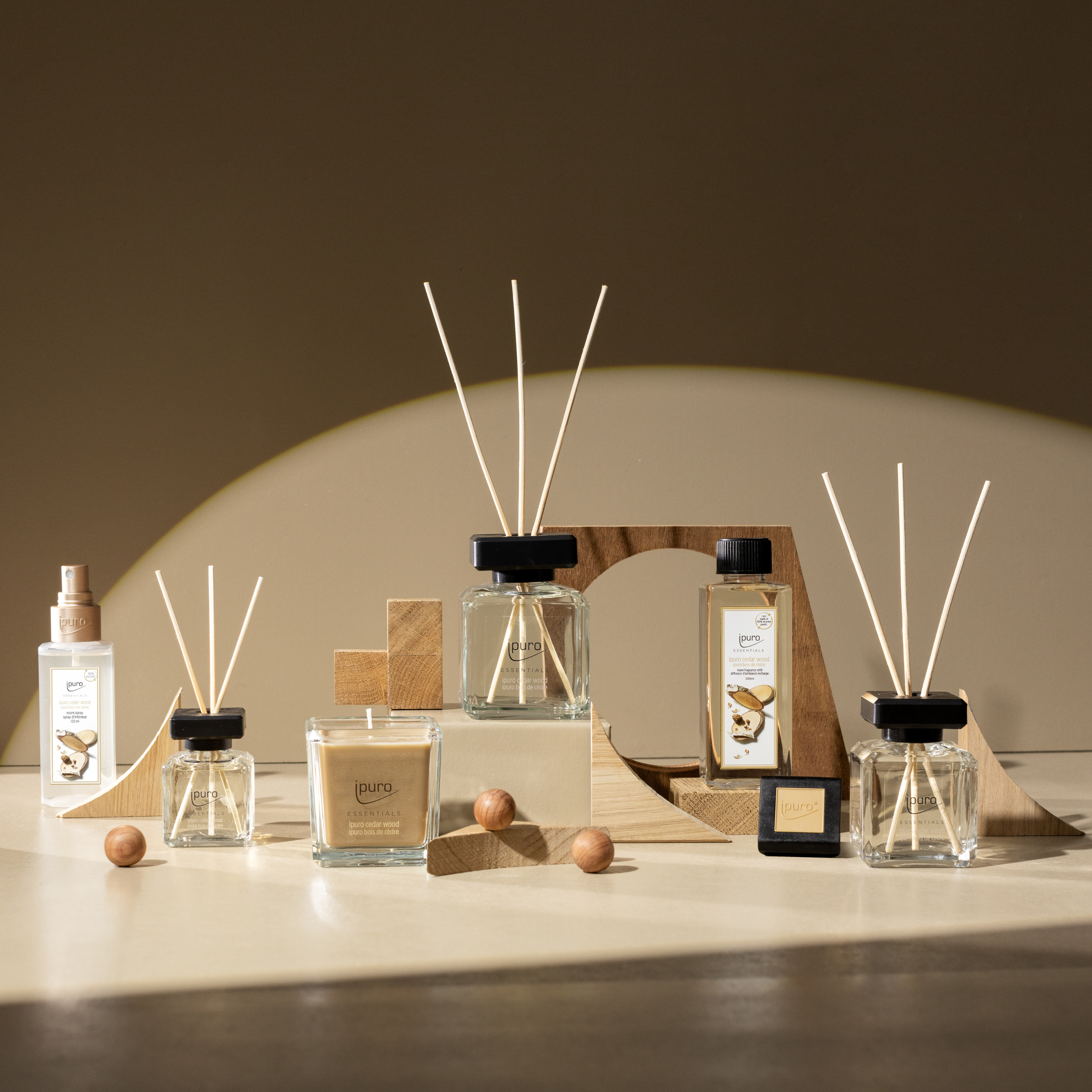 Der ESSENTIALS ipuro cedar wood Scent Plug Refill von ipuro wird auf einer beigen Oberfläche mit geometrischem Holzdekor und Kugeln präsentiert, die in sanftes natürliches Licht getaucht ist und den warmen Duft von Zedernholz und Sandelholz hervorhebt.