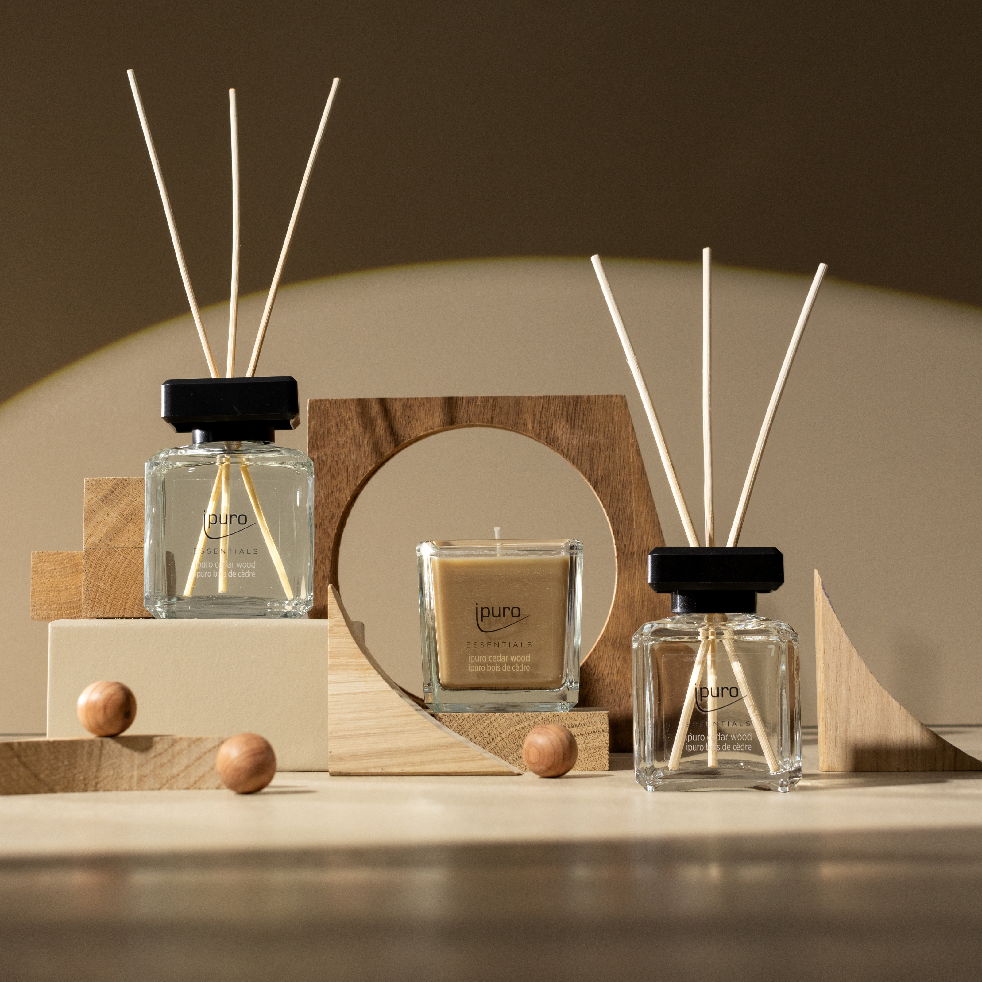Der ESSENTIALS ipuro Zedernholz Scent Plug Refill von ipuro steht zwischen geometrischen Holzformen auf einer beigen Fläche mit warmer Beleuchtung und erfüllt die Szene mit einem gemütlichen, holzigen Duft von Zedernholz und Sandelholz.