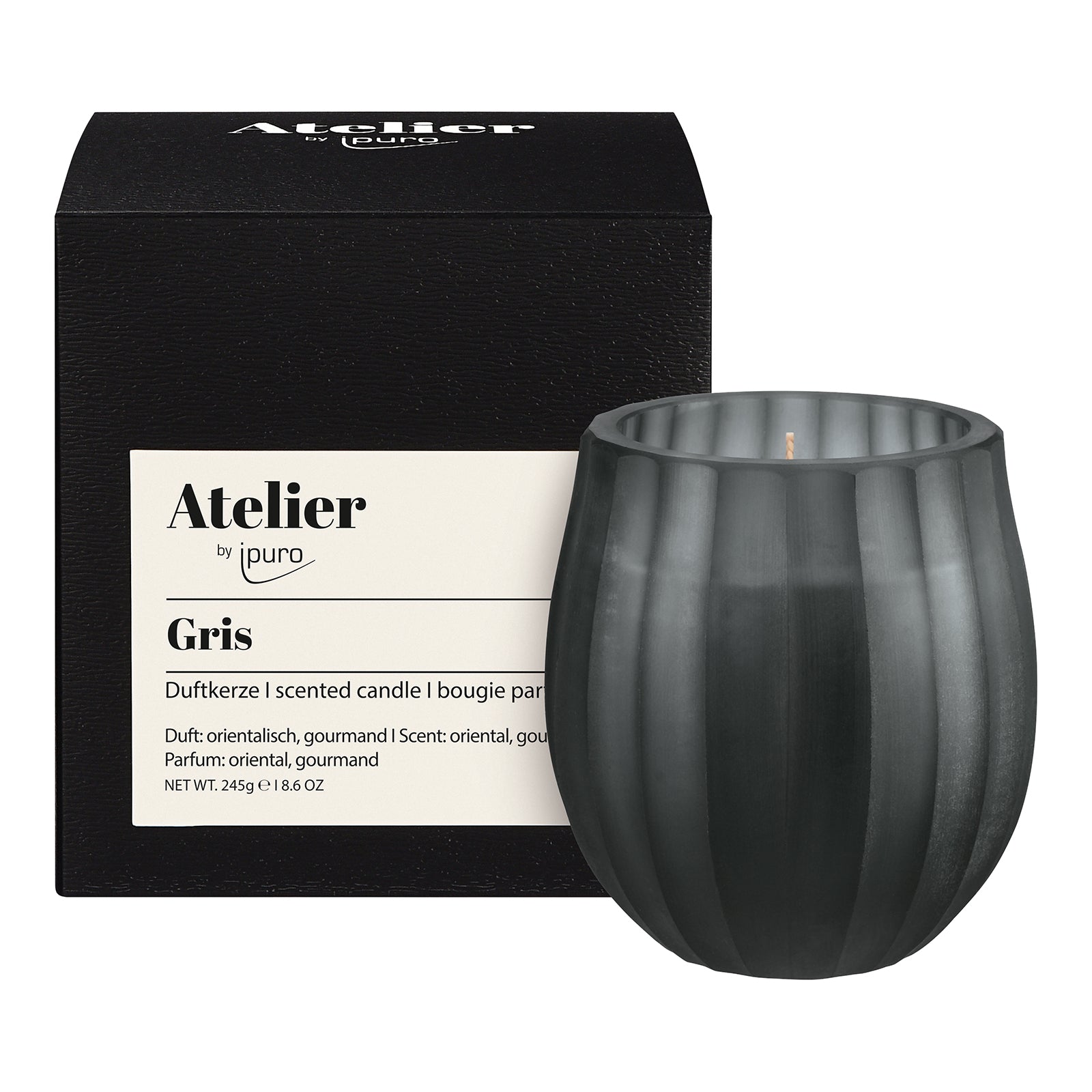 Ein schwarzer, gerippter Kerzenhalter steht neben einer schwarzen Schachtel mit der Aufschrift "Atelier by ipuro gris Duftkerze" von ipuro. Diese 245 g schwere Luxuskerze hat einen orientalischen und gourmandigen Duft.