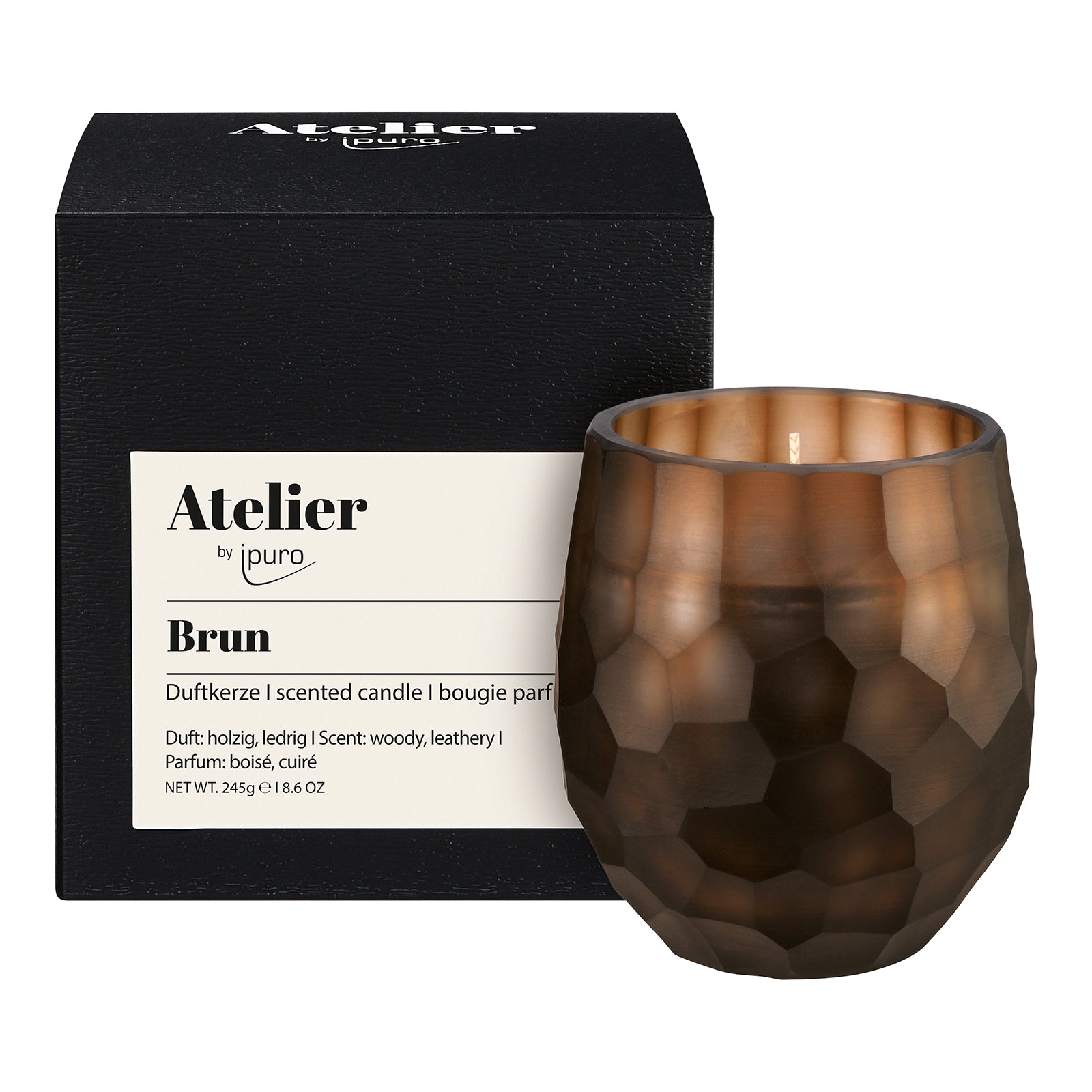 Die Atelier by ipuro brun Duftkerze von ipuro ist eine braune, facettierte Glaskerze mit holzigen und ledrigen Noten, 245g Duftwachs, abgebildet vor ihrer schwarzen Markenbox.