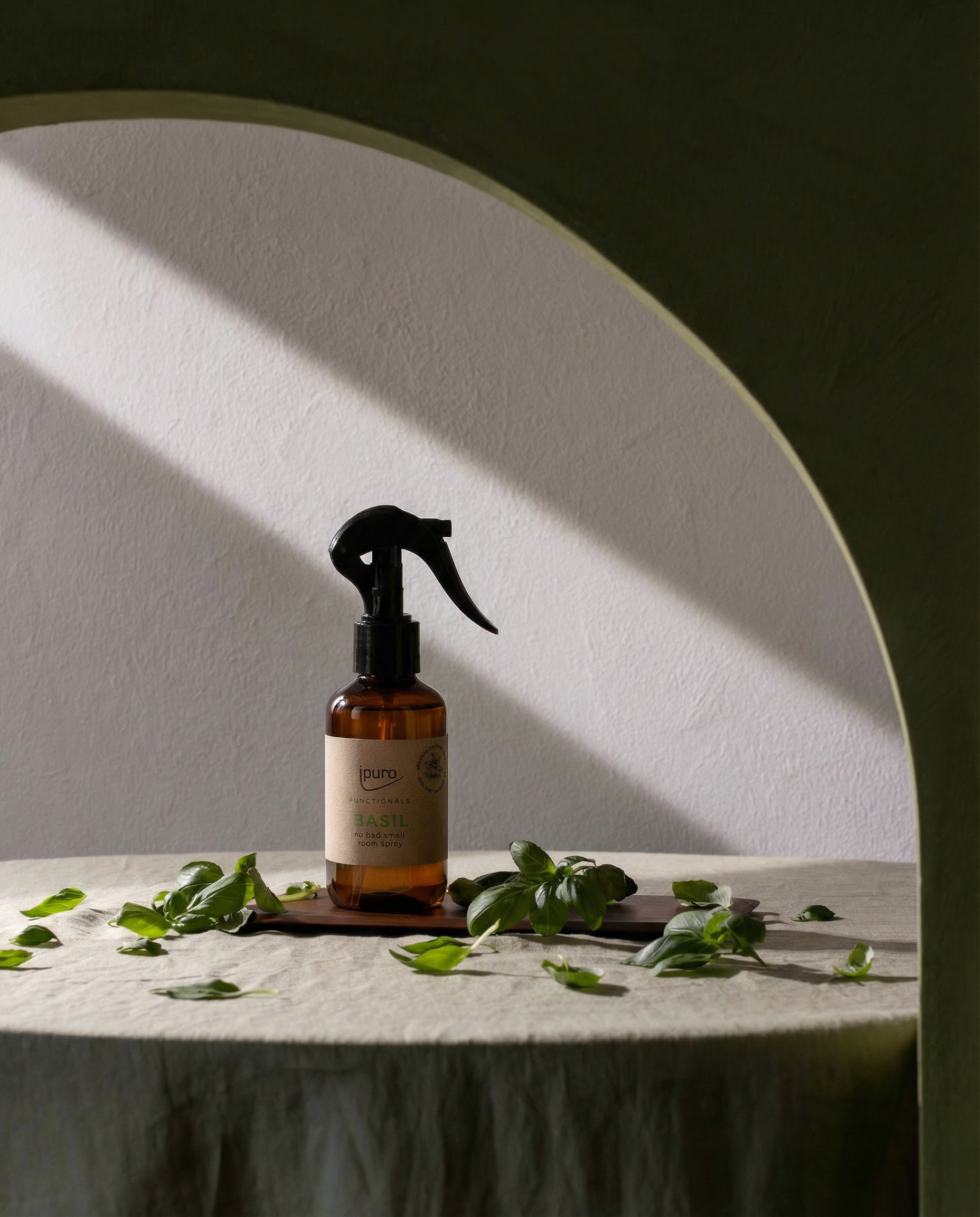 Eine 150ml FUNCTIONALS ipuro Basilikum Raumspray Flasche von ipuro ruht auf einem Stein, mit frischen Basilikumblättern in der Nähe. Das Sonnenlicht fällt durch eine gewölbte Öffnung und erzeugt weiche Schatten in dieser ruhigen Umgebung.