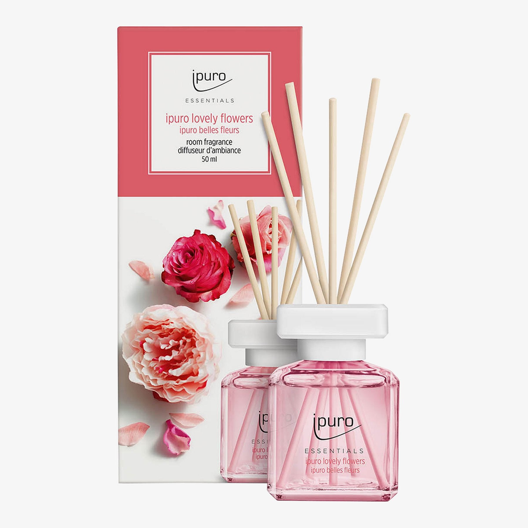 Zwei mit rosafarbener Flüssigkeit gefüllte Klarglasflaschen und Holzstäbchen stehen vor einer Blumenschachtel mit der Aufschrift ESSENTIALS ipuro lovely flowers Raumduft von ipuro, einem Raumduftzerstäuber mit einem Hauch von Rose.