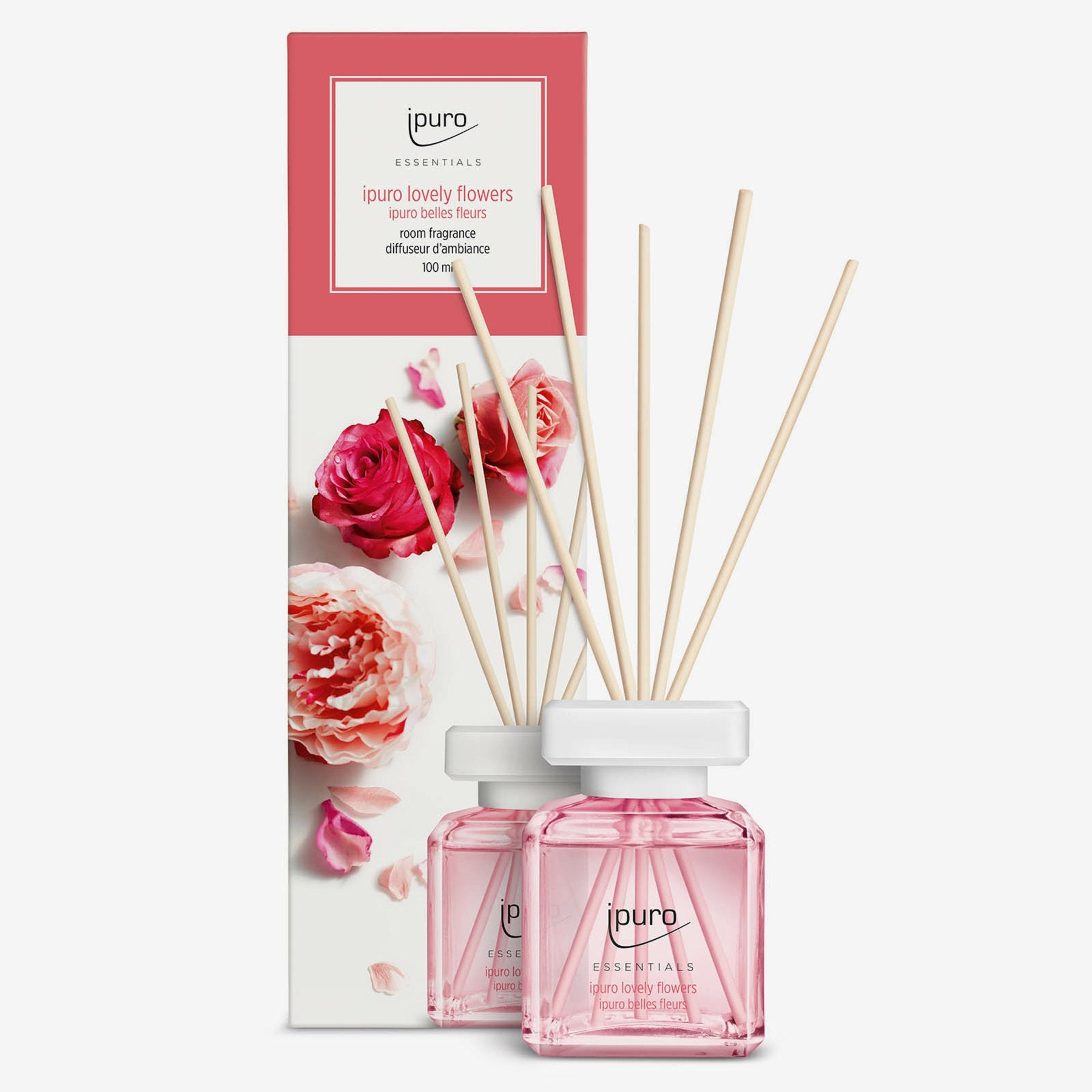 Ein Flakon von ESSENTIALS ipuro lovely flowers Raumduft von ipuro mit Holzstäbchen wird neben seiner blumengeschmückten Schachtel mit rosa und roten Blumen gezeigt. Sein herrlicher Duft enthält Noten von Rose und Maiglöckchen.