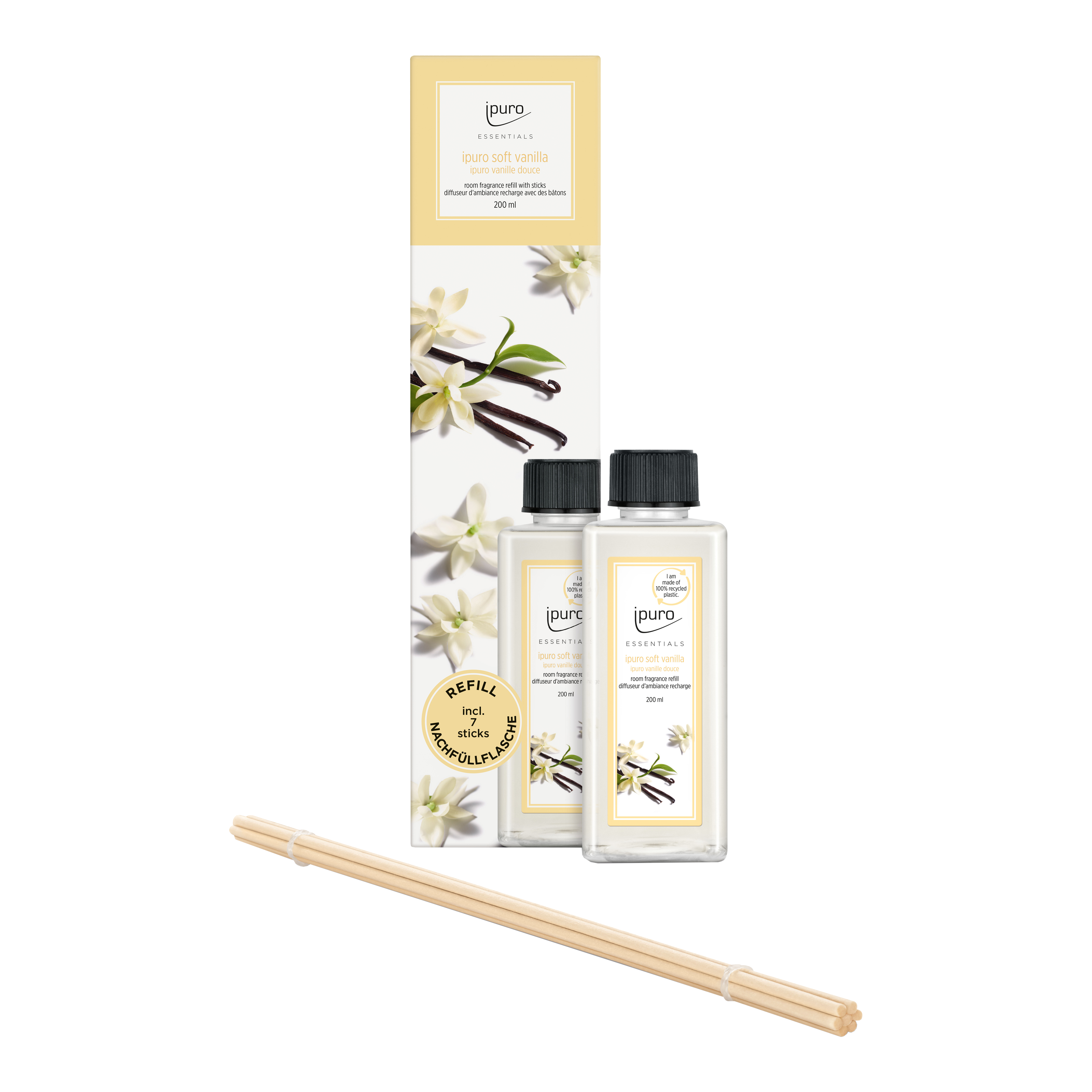 Zwei Flaschen ESSENTIALS ipuro soft vanilla Raumduft-Nachfüller und ein Bündel Holzschilf sind vor einer blumigen, mit Vanille verzierten Verpackung zu sehen. Das ipuro-Etikett hebt den reinen, weichen Vanilleduft hervor.