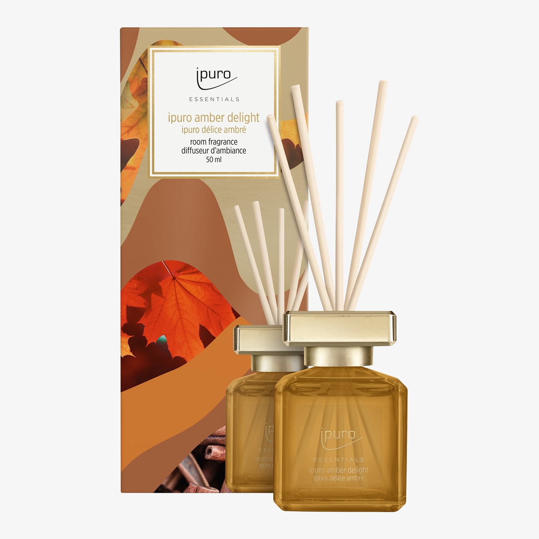 Eine Flasche ESSENTIALS ipuro Amber Delight Raumduft mit weißem Schilf steht vor ihrer herbstlich gestalteten Verpackung in Braun- und Orangetönen von ipuro.