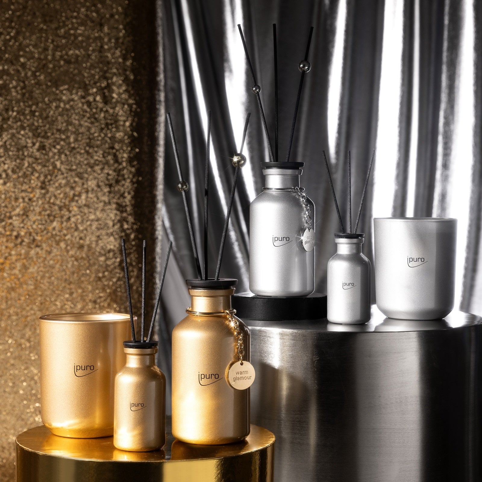 Ein Display aus gold- und silberfarbenen ipuro LIMITED EDITION warm glamour & cold glamour Geschenk-Sets auf metallischen Sockeln, unterlegt mit schimmernden gold- und silberfarbenen Stoffen - perfekt, um einen Hauch von Winterduft zu erzeugen.