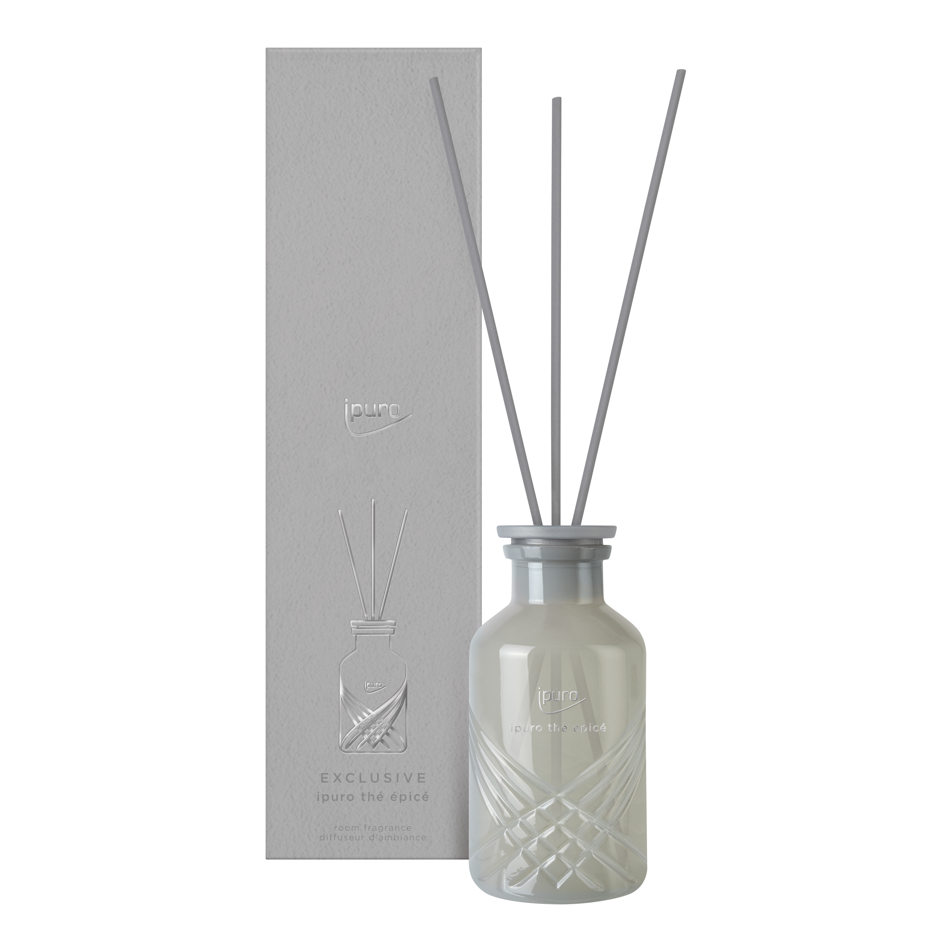 Ein weißer Glasschilfdiffusor, EXCLUSIVE ipuro thé epicé Raumduft by ipuro, mit drei grauen Schilfrohren steht vor seiner passenden, geprägten Box - beide mit dem ipuro-Branding.