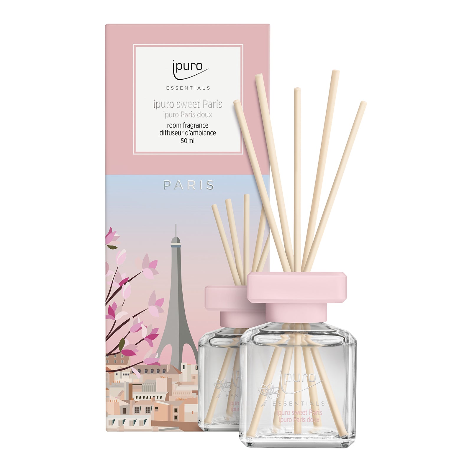 Zwei ESSENTIALS ipuro sweet paris Raumduft-Diffusoren aus Glas mit rosafarbenen Deckeln und Holzstäben werden vor einer Pariser Themenbox mit Kirschblüten und dem Eiffelturm präsentiert. Sie enthalten jeweils 50 ml ipuro Raumduft mit Vanillearoma.
