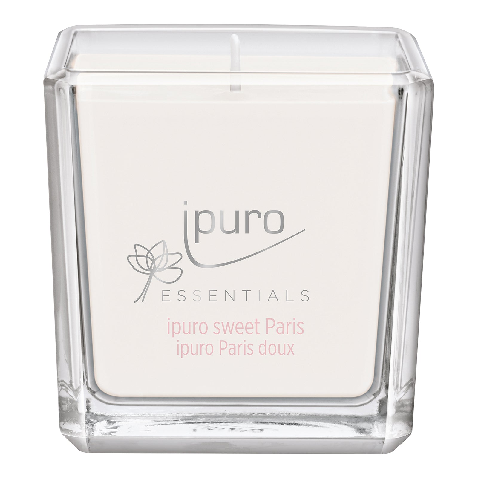 Eine quadratische, klare Glaskerze mit weißem Wachs und einem Etikett mit ipuro ESSENTIALS und Blumenkunst. Die ESSENTIALS ipuro sweet paris Duftkerze von ipuro bietet ein blumiges Aroma mit Noten von Vanille, etikettiert in rosa und grau.