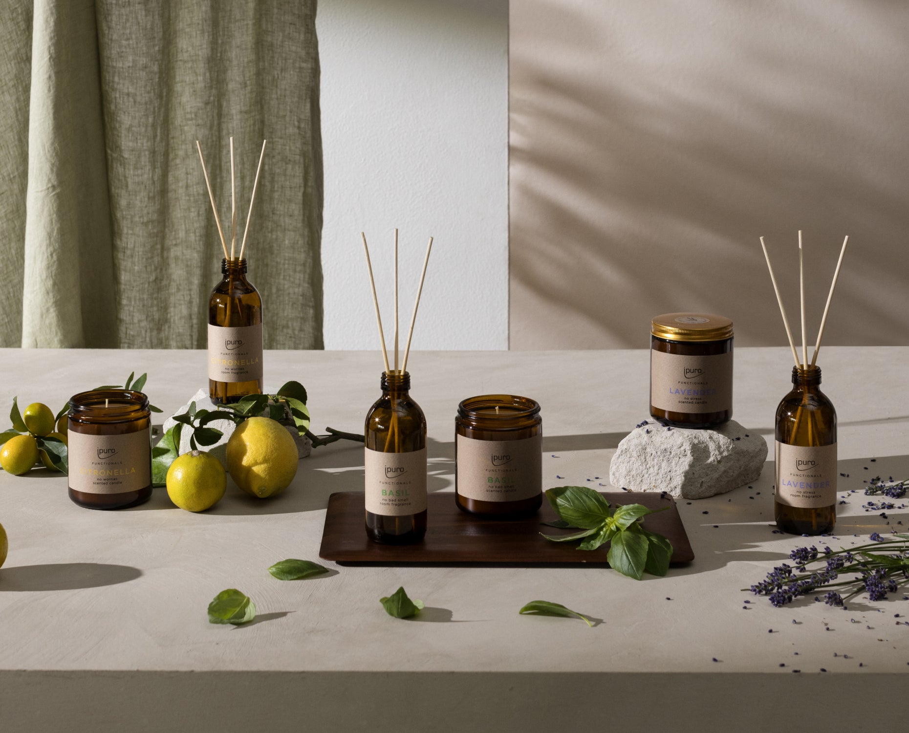 Braunglasgefäße und Rohrdiffusoren stehen auf einem hellen Tisch mit frischen Zitronen, grünen Blättern und einem Stein in der Nähe. Getrockneter Lavendel und ein grüner Vorhang stehen im Hintergrund und schaffen eine natürliche, spa-ähnliche Umgebung.