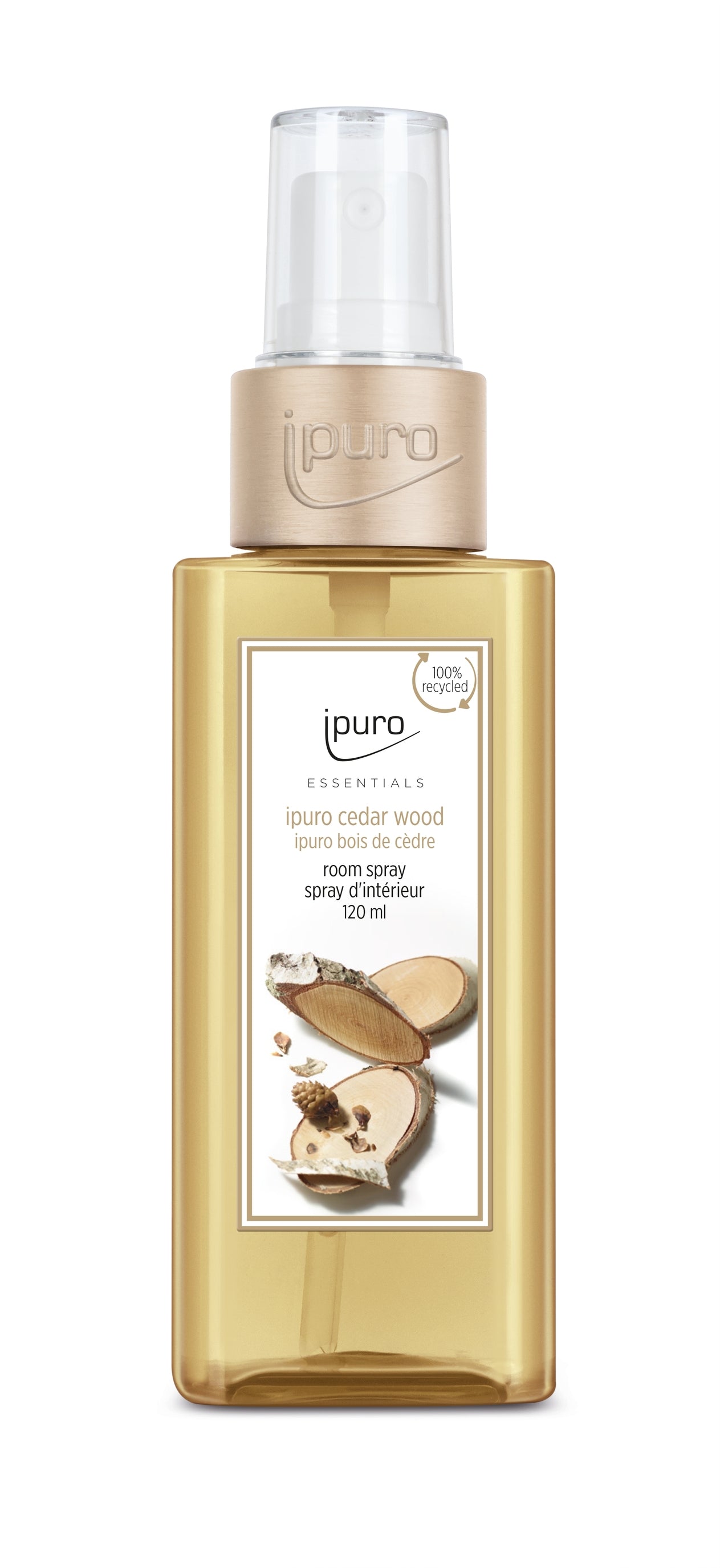 A 120 ml transparent amber ESSENTIALS ipuro cedar wood Raumspray with a beige cap and label showing Zedernholz slices. Made from 100% recycled material, it features Holzige Noten.