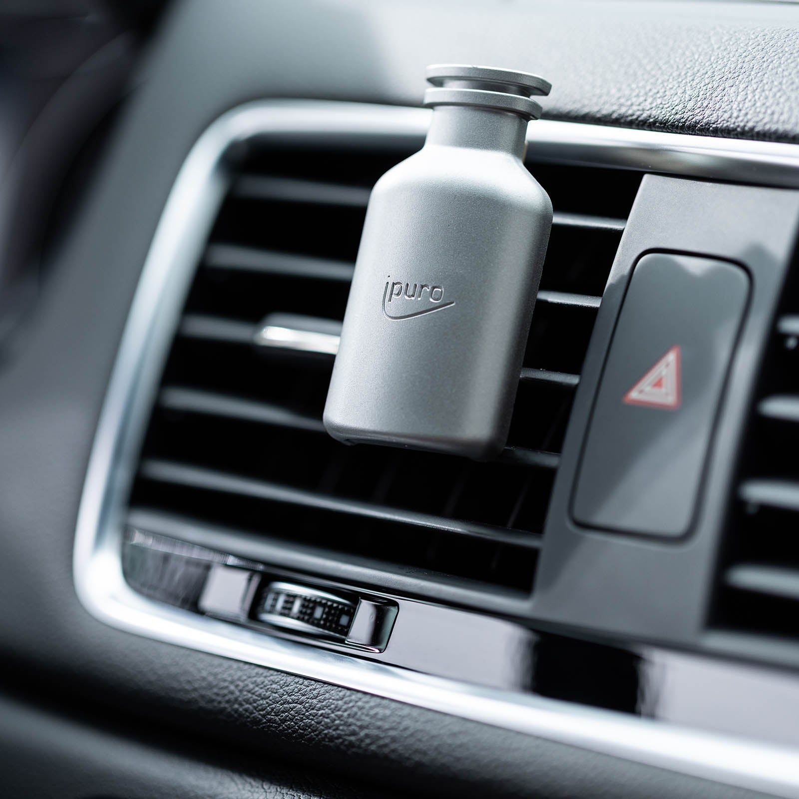 Eine Nahaufnahme einer Auto-Luftklappe mit einem silbernen ipuro CLASSIC blanc Autoduft Nachfüllpack von ipuro, das einen Hauch von Minze aufweist. Das Armaturenbrett und der Warnblinkerknopf sind ebenfalls zu sehen.
