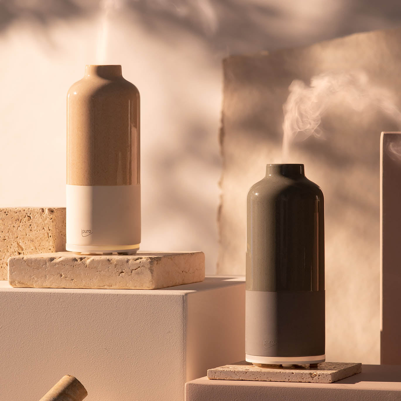 Zwei AIR SONIC ipuro aroma bottle Elektrischer Aroma-Diffusoren von ipuro, ausgestattet mit Ultraschalltechnologie, verdampfen über strukturierten Steinblöcken. Einer ist beige und weiß, der andere dunkelgrün und grau und schafft ein ruhiges, minimalistisches Ambiente mit sanfter Beleuchtung.