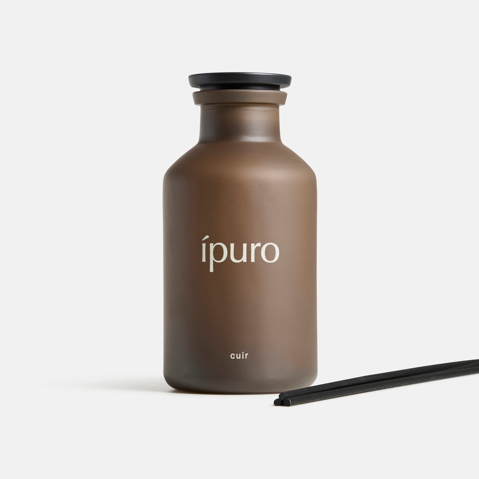 Ein brauner Milchglasflakon mit schwarzer Kappe von ipuro mit der Aufschrift "Raumduft ipuro cuir" enthält zwei schwarze Diffusorstäbchen - eine elegante Ergänzung, um Ihren Raum mit Vanille- und Zitrusnoten zu beduften.