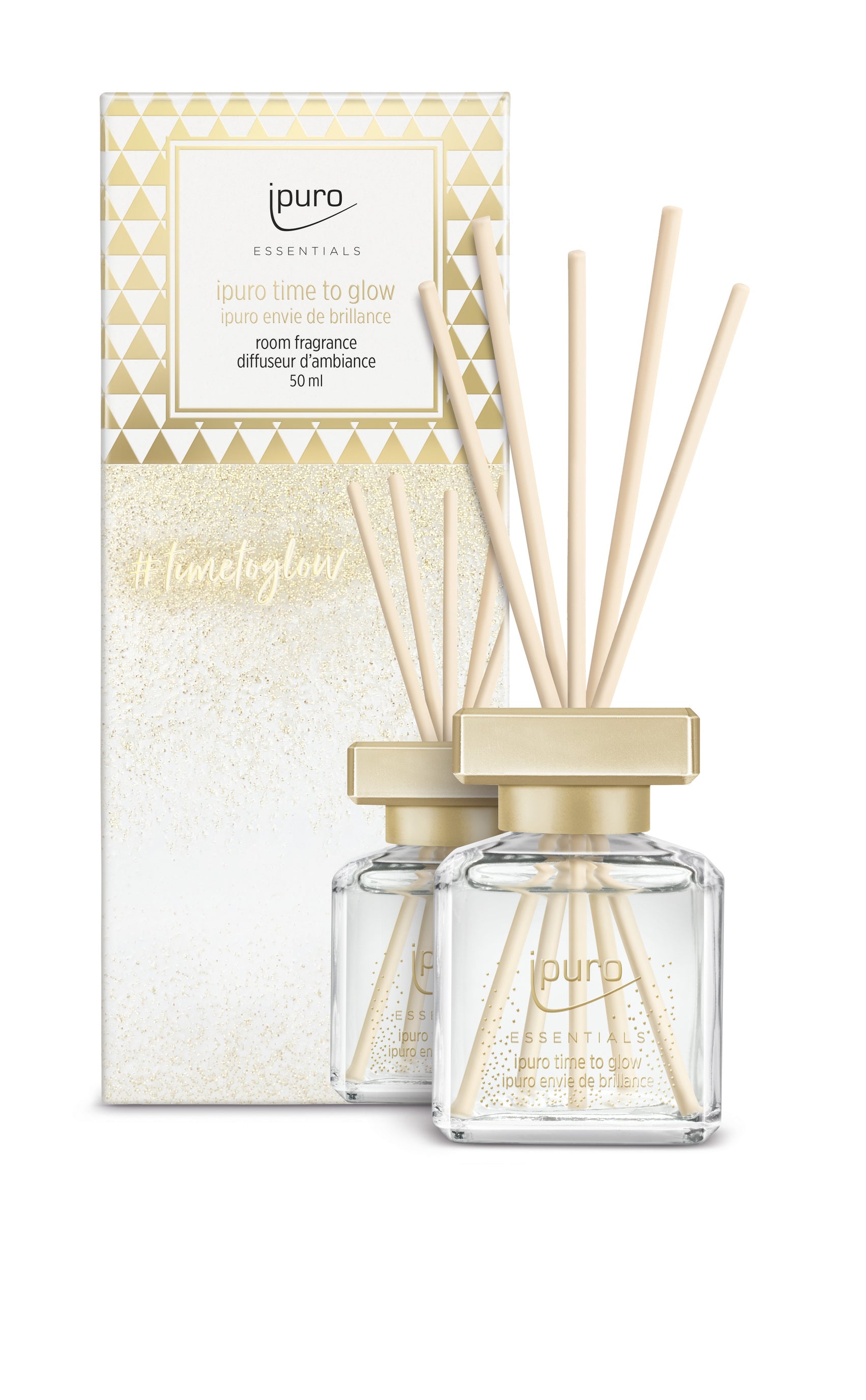 Ein Set von zwei ESSENTIALS ipuro time to glow Raumduft Diffusoren von ipuro aus Klarglas mit goldenen Kappen und hellen Schilfblättern, die orientalische Blumennoten wie Kaschmirholz und Tonkabohne enthalten, vor einer passenden geometrischen Box in Weiß und Gold.