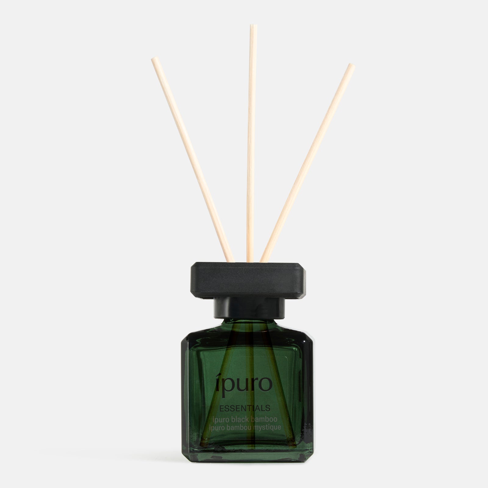 Der Raumduft ipuro black bamboo diffuser bottle von ipuro aus grünem Glas mit drei Holzstäben in einer schwarzen Kappe erinnert an grüne Frische und holzige Nuance vor einem schlichten weißen Hintergrund.
