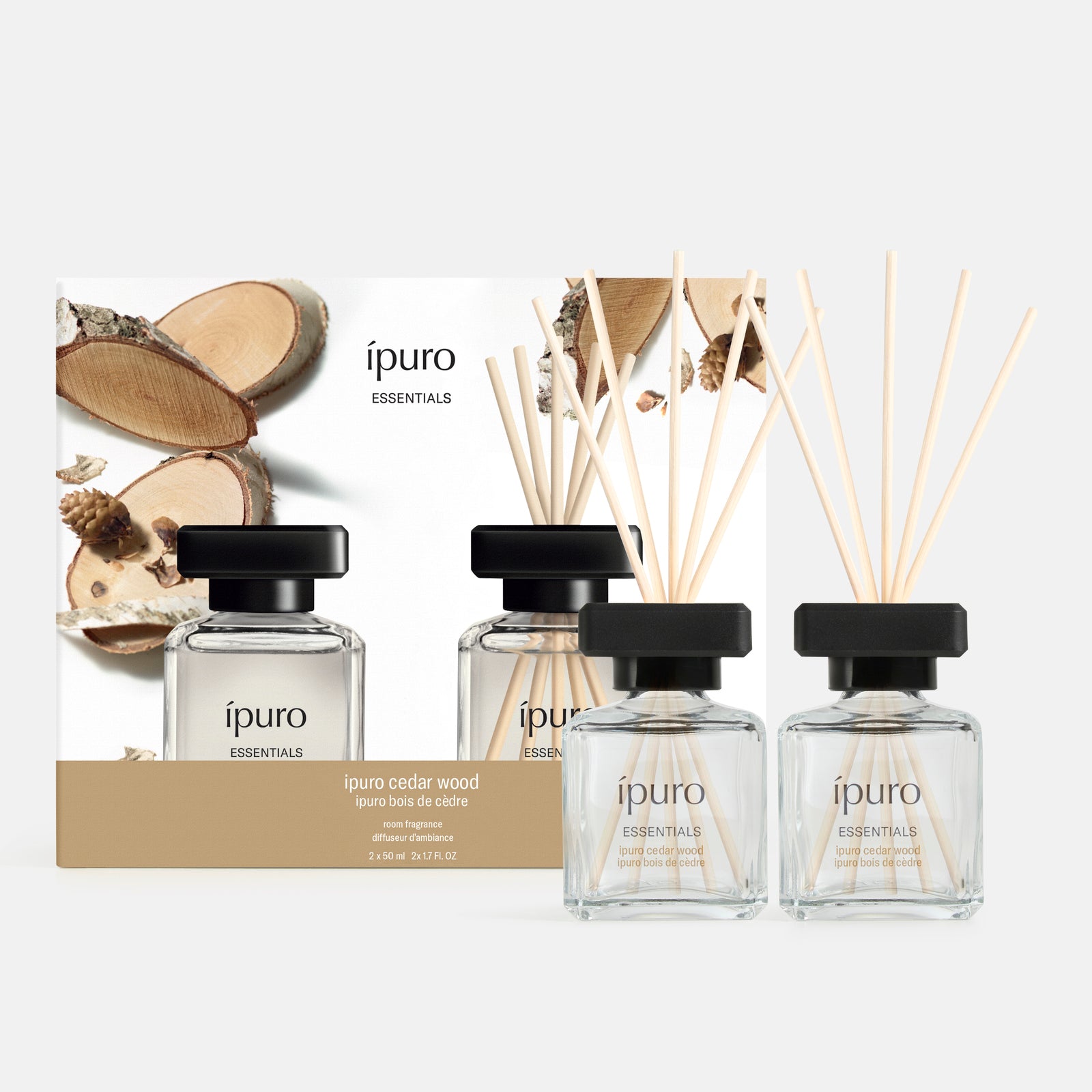 Zwei Raumduft-Sets aus ipuro-Zedernholz stehen vor ihrer mit Holz- und Kiefernzapfenmotiven verzierten Box. Sie haben schwarze Kappen und Holzschilf und füllen Ihren Raum mit einem entspannenden Himalaya-inspirierten Waldduft.