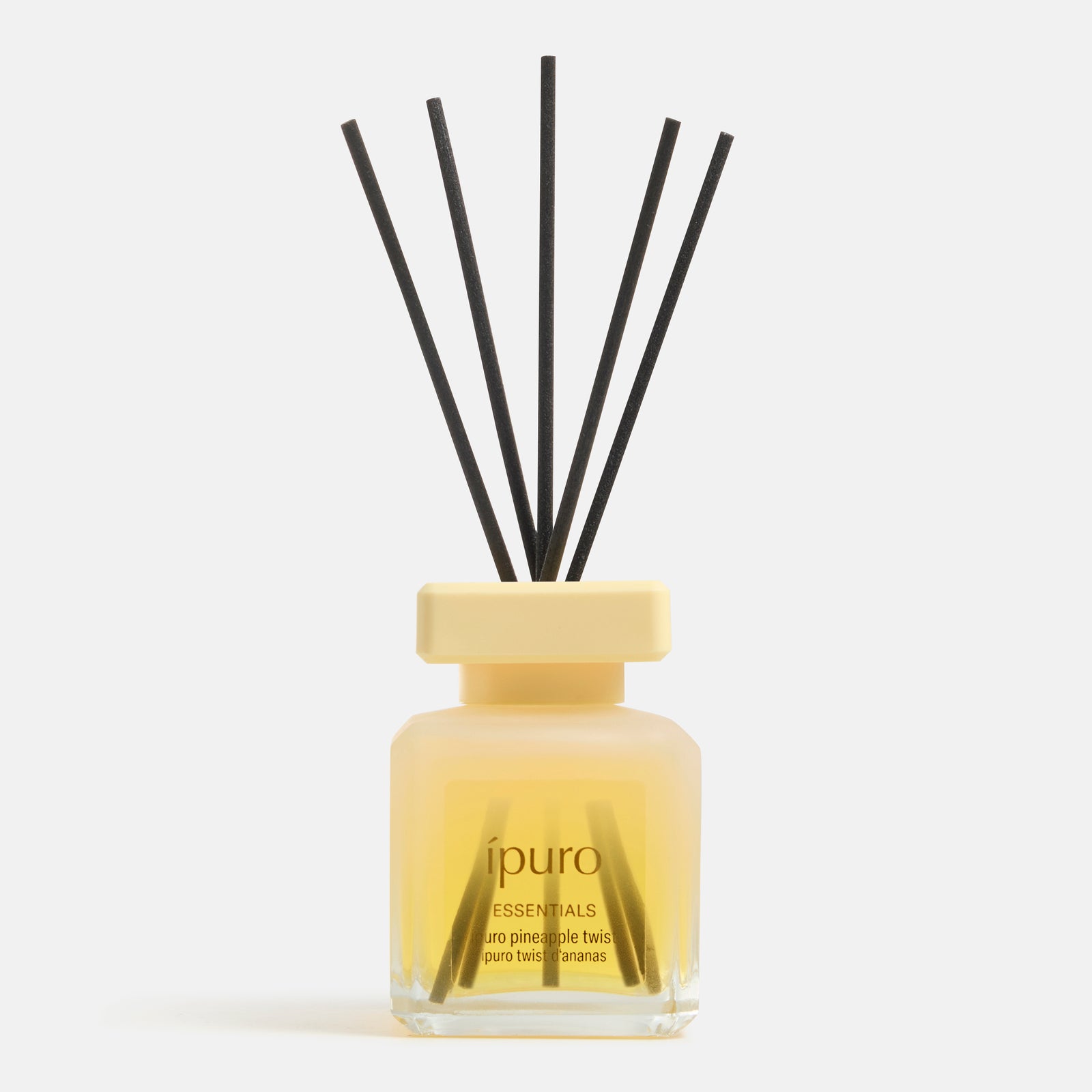 Eine Glasflasche mit gelbem Deckel und der Aufschrift "ipuro ESSENTIALS pineapple twist" von ipuro, mit schwarzen Schilfrohrstäbchen und gelber Duftflüssigkeit, bringt einen frischen Ananasduft und ein tropisches Aroma in Ihren Raum.