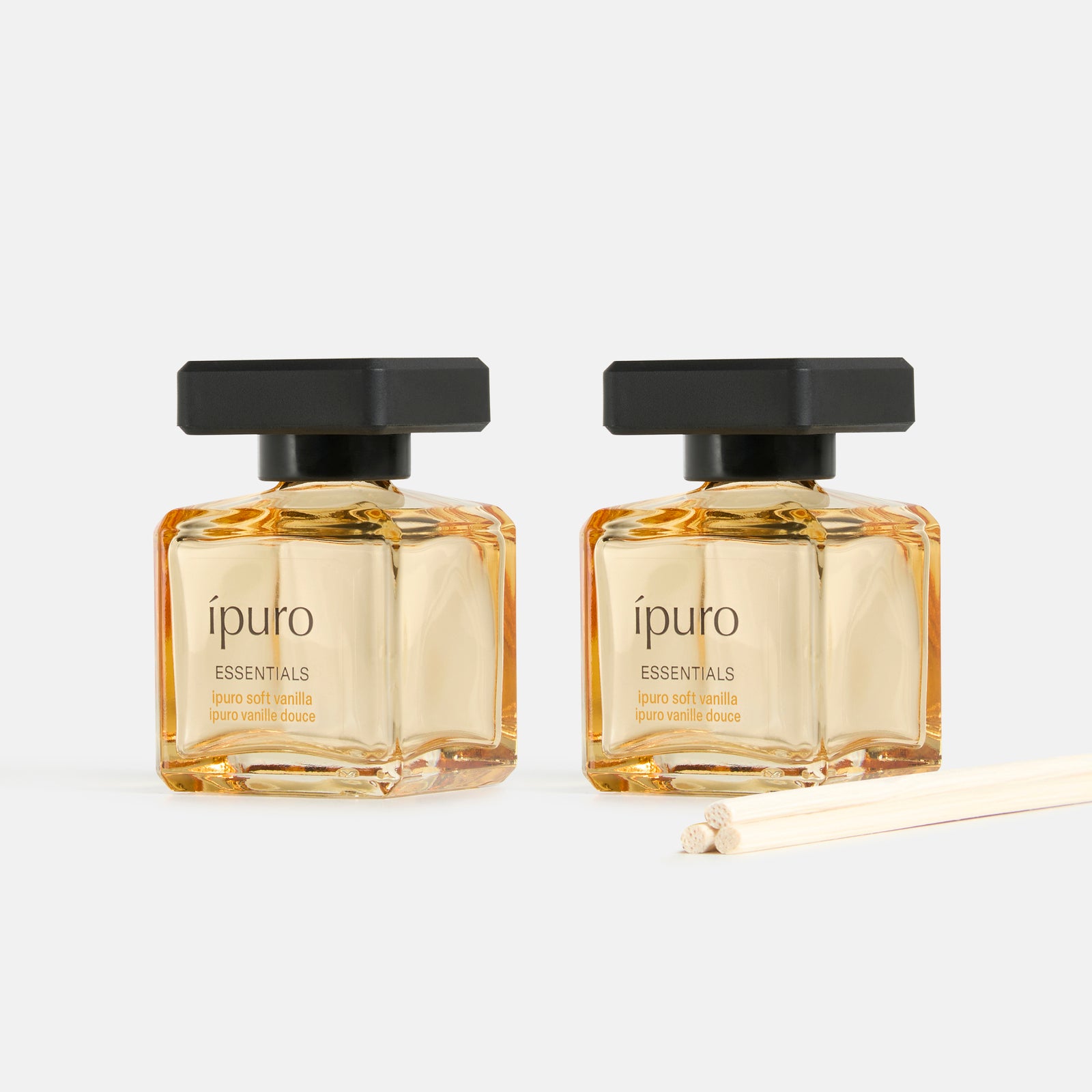 Zwei quadratische Glasflakons aus dem ipuro Raumduft-Set soft vanilla mit schwarzem Verschluss und dünnen Holzstäbchen stehen nebeneinander auf hellem Grund, untermalt von Noten von Vanille und Sandelholz.