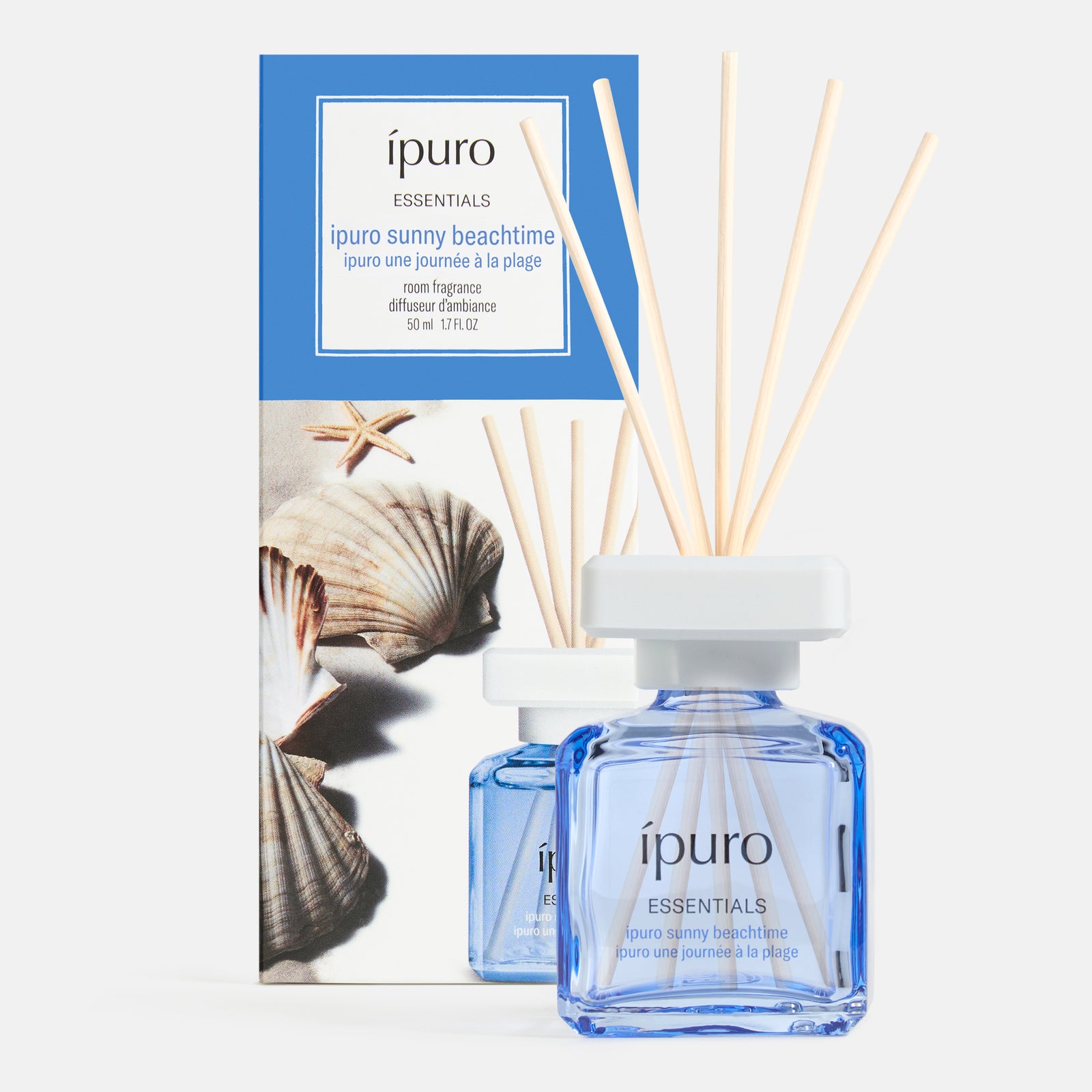 Ein blauer Glasflakon des ipuro Raumduft sunny beachtime Schilfrohrdiffusors mit Holzstäbchen steht vor seiner mit Muscheln und Seesternen verzierten Box und fängt die Essenz von Sommer am Strand unter der Sonne von ipuro ein.