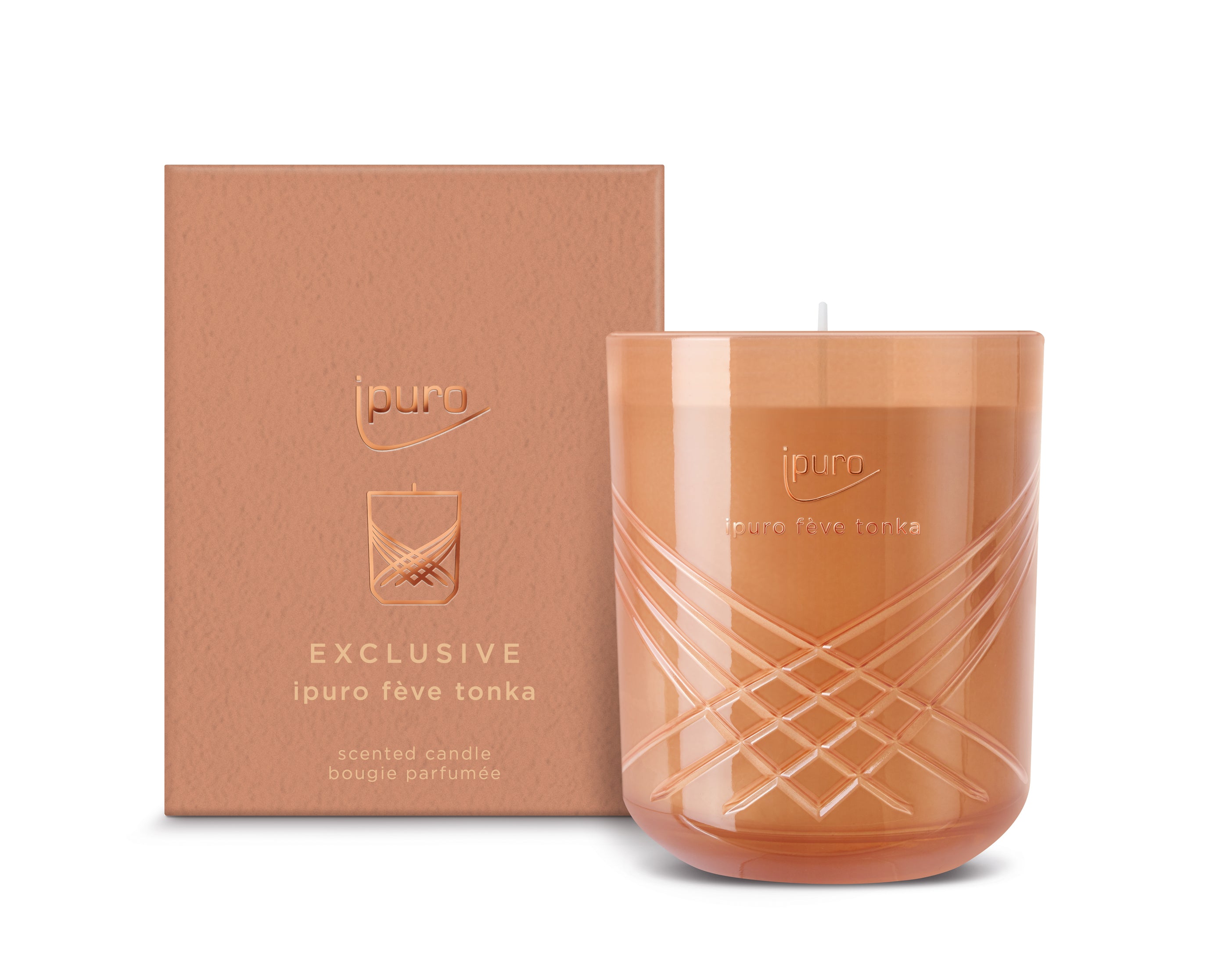 Eine orange-braune EXCLUSIVE ipuro fève tonka Duftkerze von ipuro mit Noten von Tonkabohne und Sandelholz ruht in einem dekorativen Glashalter neben der passenden Schachtel - beide verziert mit goldenen Marken- und Produktangaben.