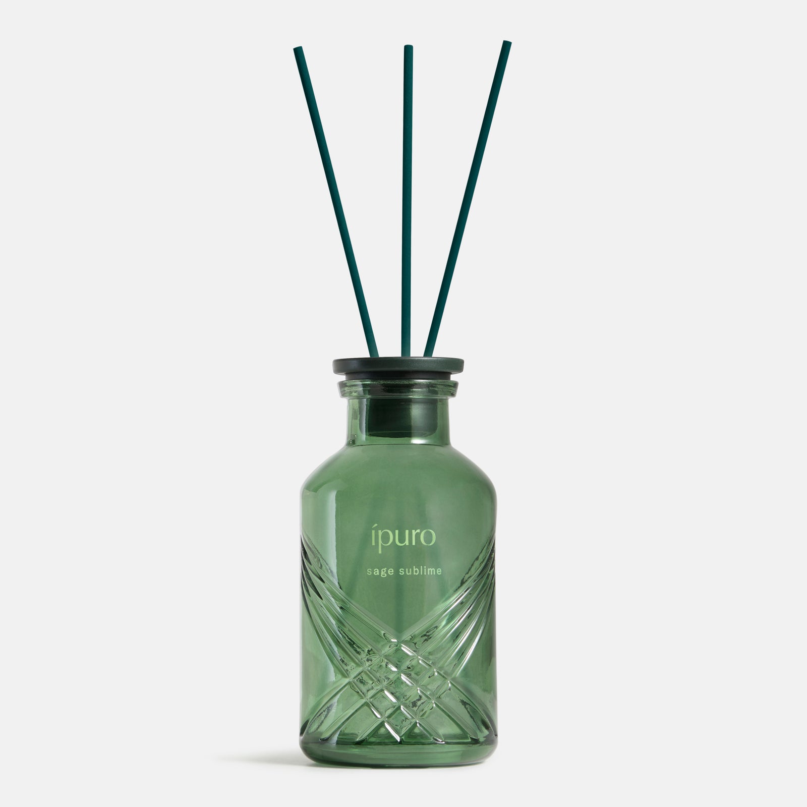 Ein grüner Glasflakon mit der Aufschrift "ipuro sage sublime Raumduft" von ipuro mit drei dunklen Schilfrohren auf weißem Grund - sein Duft verbindet Salbei und mineralische Noten zu einer sinnlichen Komposition.