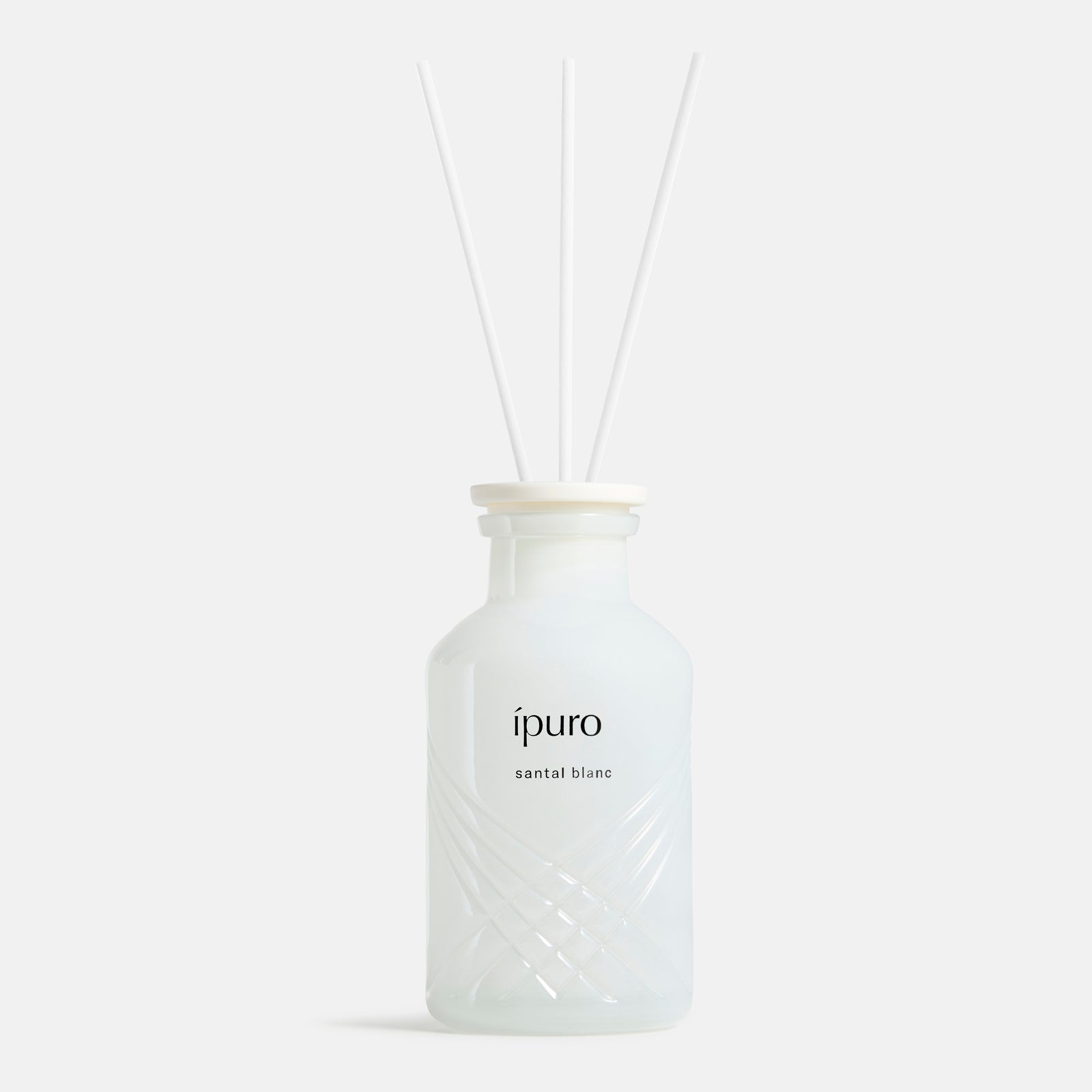 Der mattweiße ipuro santal blanc Raumduft Diffusor von ipuro mit drei weißen Schilfstäbchen verbreitet Düfte von Sandelholz und weißer Orchidee vor einem schlichten, hellen Hintergrund.