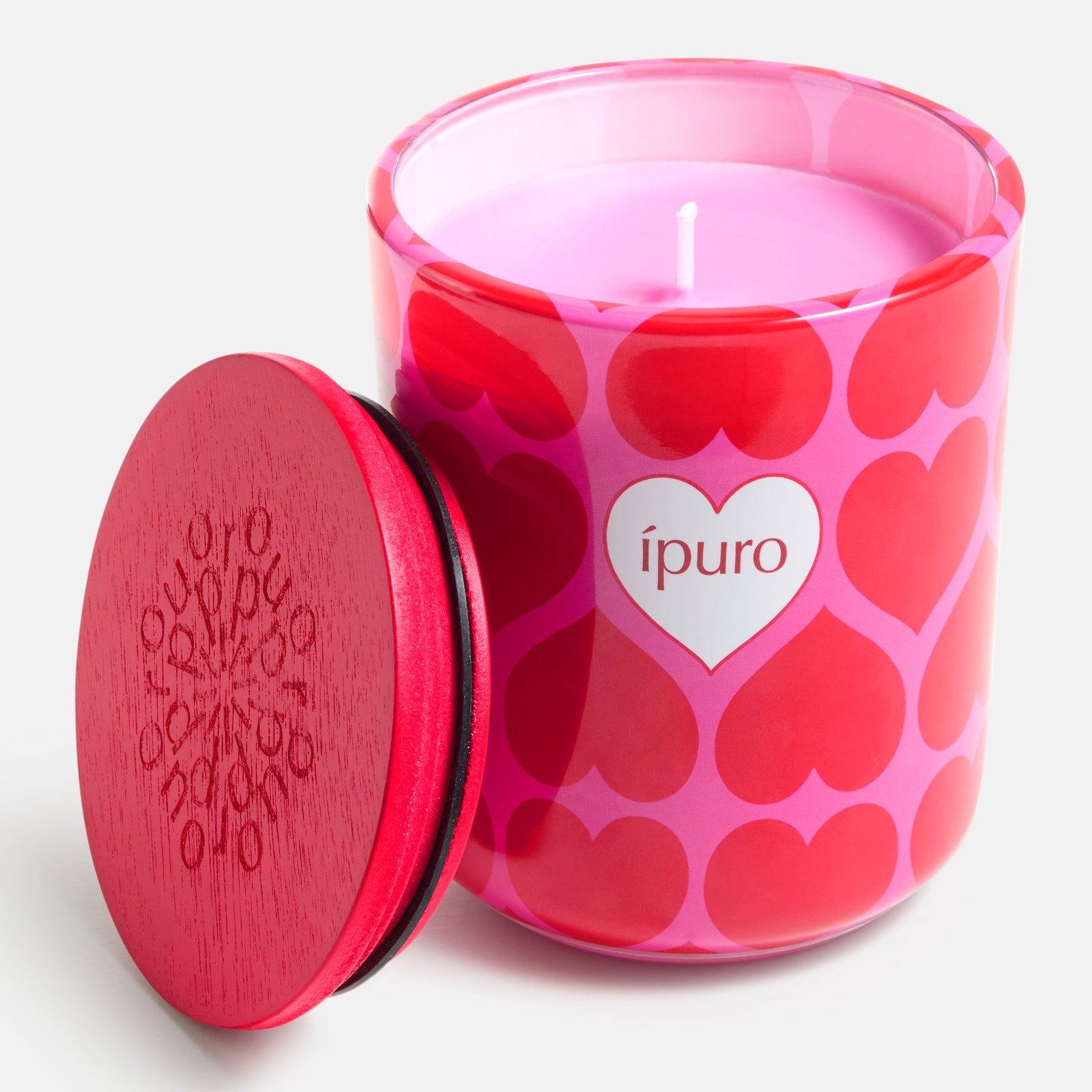 Die LIMITED EDITION ipuro love's embrace Kerze 270g von ipuro ist eine rosafarbene Kerze in einem Glasgefäß mit roten Herzmustern, einem weißen herzförmigen "ipuro"-Etikett, Kokosnuss-Noten und wird mit einem roten Holzdeckel daneben geliefert.