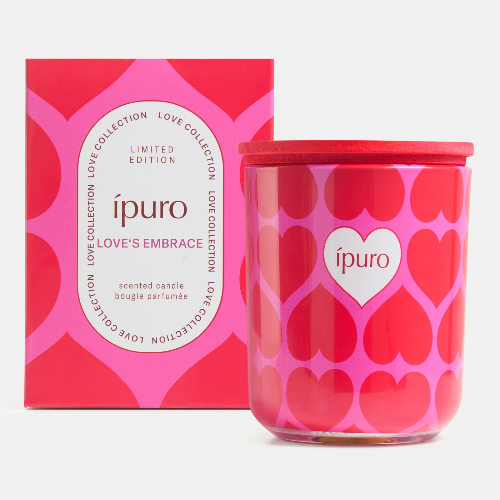 Eine rosa-rote LIMITED EDITION ipuro love's embrace Kerze 270g in einem Glastiegel mit Herzmotiv steht neben der passenden Schachtel, auf der in weißer Schrift "ipuro" und die Duftnoten von Moschus & Sandelholz zu lesen sind.