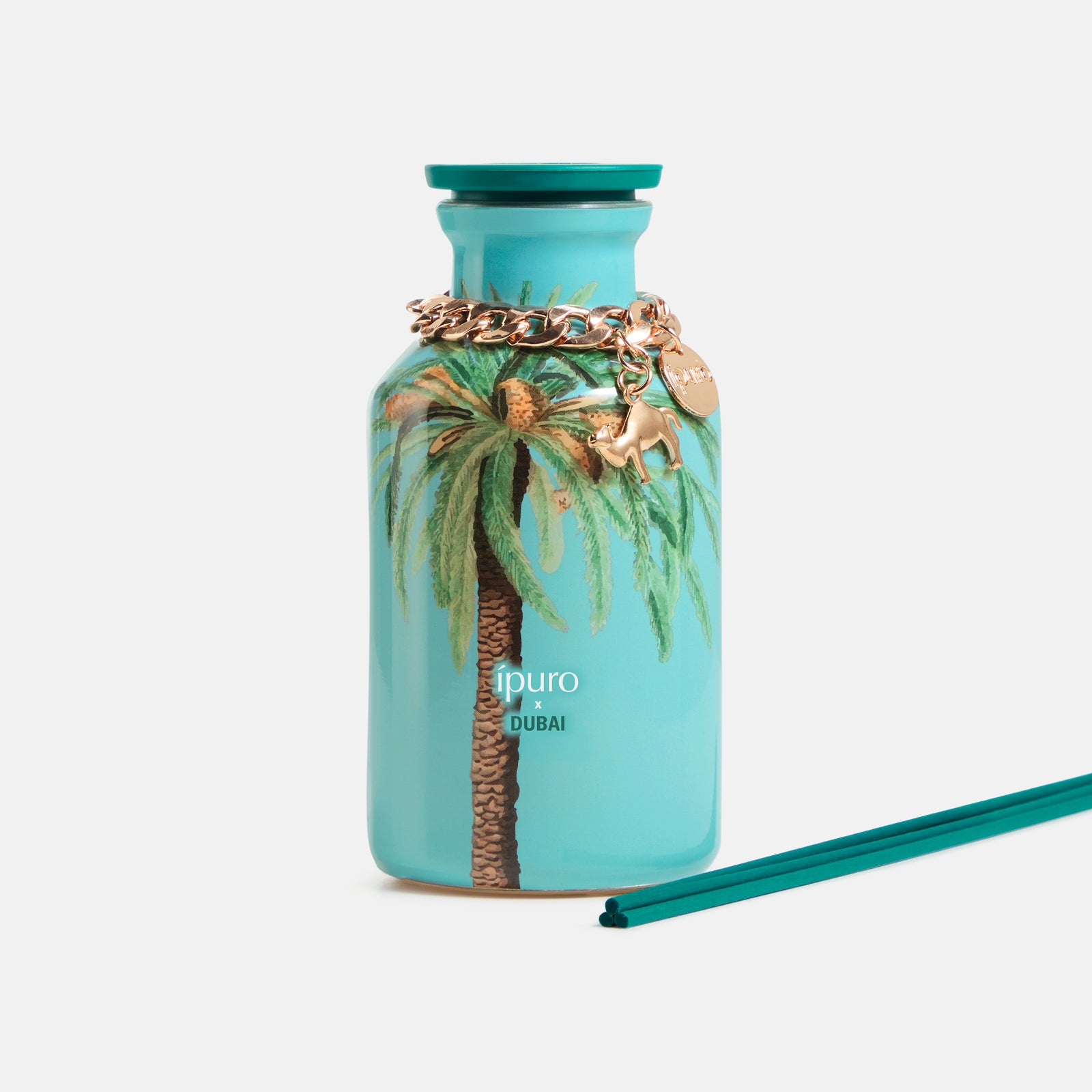 Ein türkisfarbener LIMITED EDITION ipuro x DUBAI Raumduft 240ml Flakon mit Palmenmotiv, goldener Kette und Anhängern, sowie tealfarbenen Stäbchen. Mit orientalischem Sandelholzduft von ipuro auf weißem Hintergrund.