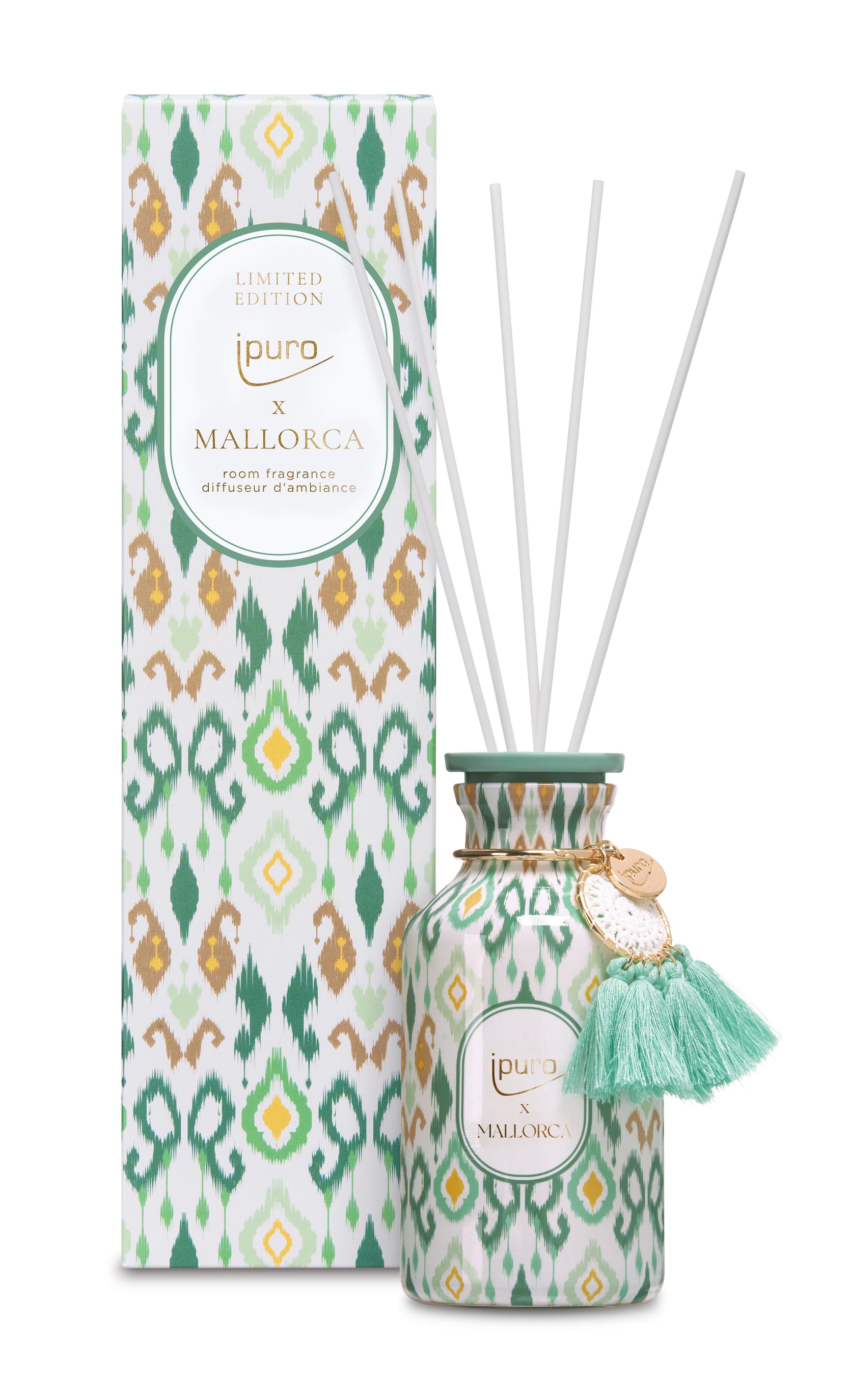Ein dekorativer Flakon des Raumduftes Ipuro x Mallorca mit weißen Diffusorstäbchen, mit grünem und goldenem Ikat-Muster, einem goldenen Anhänger und einer grünen Quaste, abgebildet neben der passenden gemusterten Schachtel.