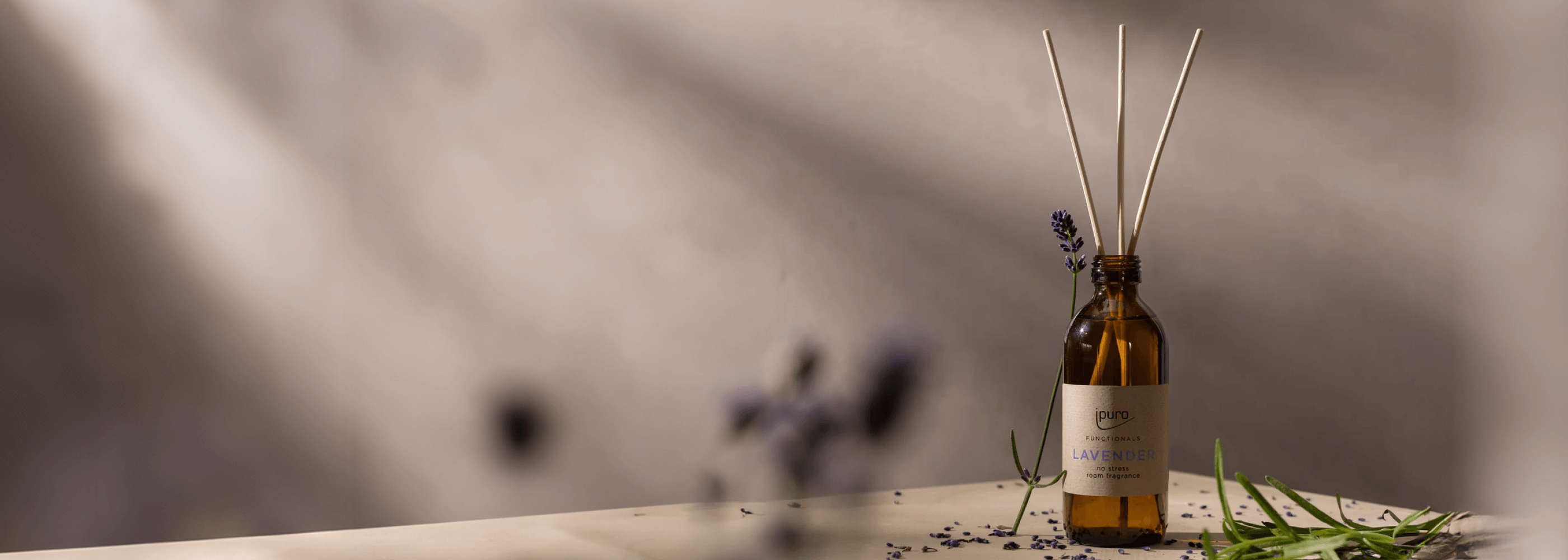 Eine Sammlung von nach Lavendel duftenden Produkten, darunter Kerzen, Diffusoren, ein Spray und ein Flakon, arrangiert auf einer Fläche mit Lavendelzweigen und violetten Akzenten in sanfter Beleuchtung.