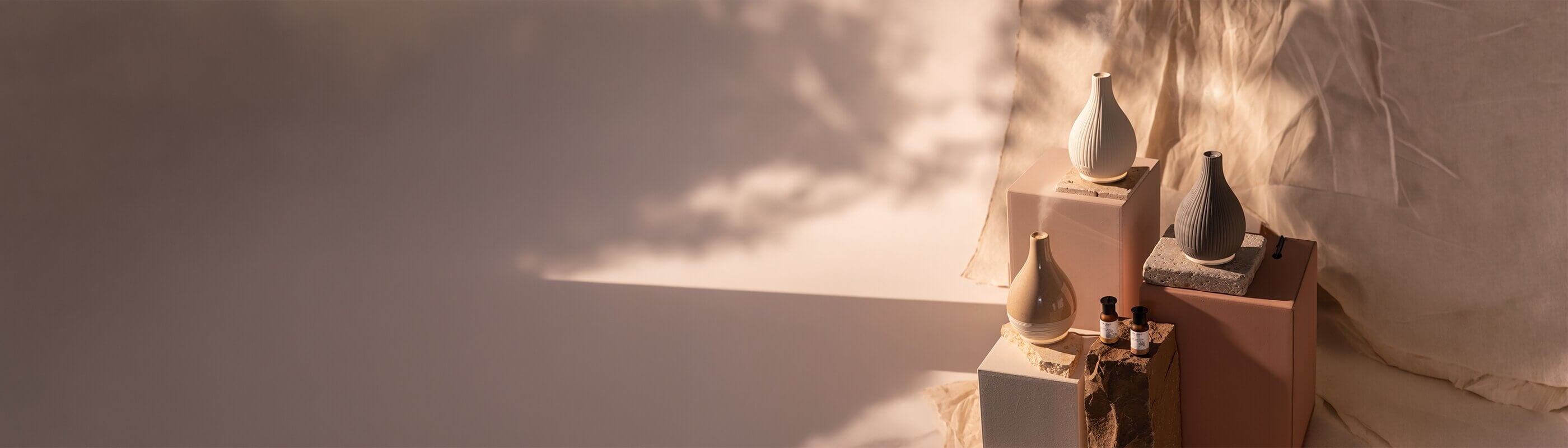 Vier Keramikvasen und zwei kleine Glasflaschen werden auf strukturierten Ständern präsentiert, wobei weiche Schatten und warmes Licht eine künstlerische, minimalistische Atmosphäre schaffen.