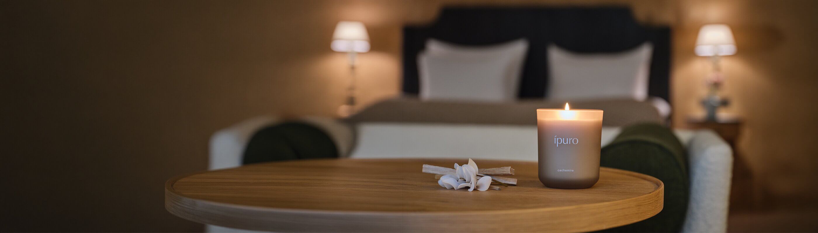 Eine brennende grüne Ipuro-Bergamotte-Kerze steht auf einer grauen Marmorarbeitsplatte neben einer ganzen Limette, zwei Limettenspalten und Braungläsern, im Hintergrund ein dunkles Steinwaschbecken.