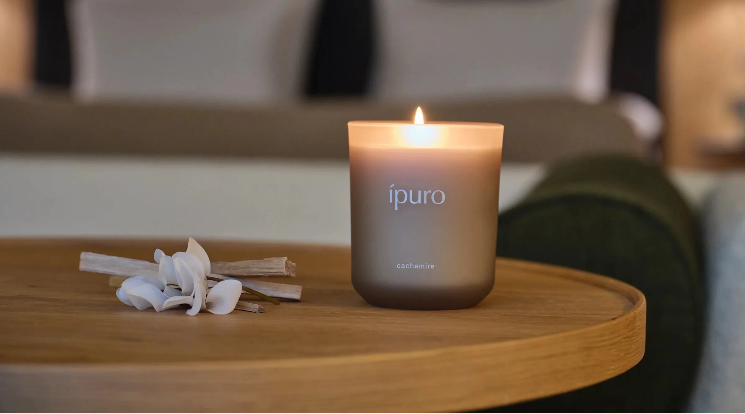 Eine brennende grüne Ipuro-Bergamotte-Kerze steht auf einer grauen Marmorarbeitsplatte neben einer ganzen Limette, zwei Limettenspalten und Braungläsern, im Hintergrund ein dunkles Steinwaschbecken.