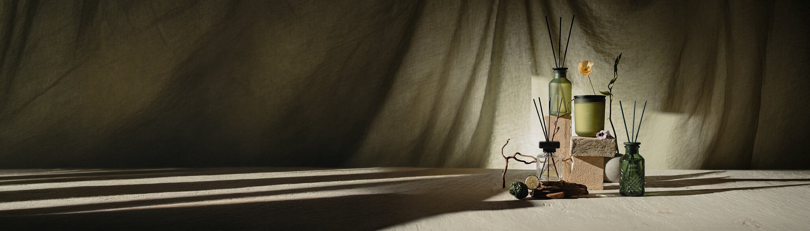 Eine rosafarbene Flasche mit schwarzen Schilfrohrstäbchen steht auf einer weißen Fläche im Freien, mit hohen grünen Bäumen und verschwommenen Gebäuden im Hintergrund.
