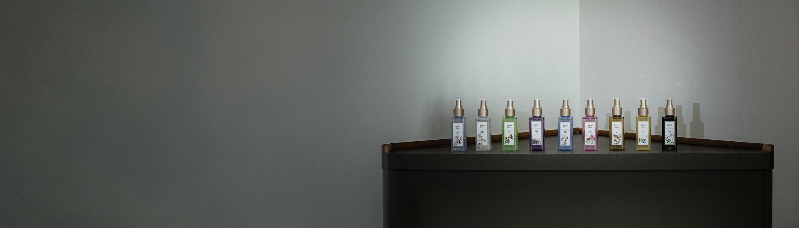 Zwölf farbenfrohe Sprühflaschen mit Körpernebel sind in einer Reihe auf einer weißen Fläche angeordnet, jede mit einem anderen Etikett und einer anderen Farbe, die für verschiedene Düfte stehen.