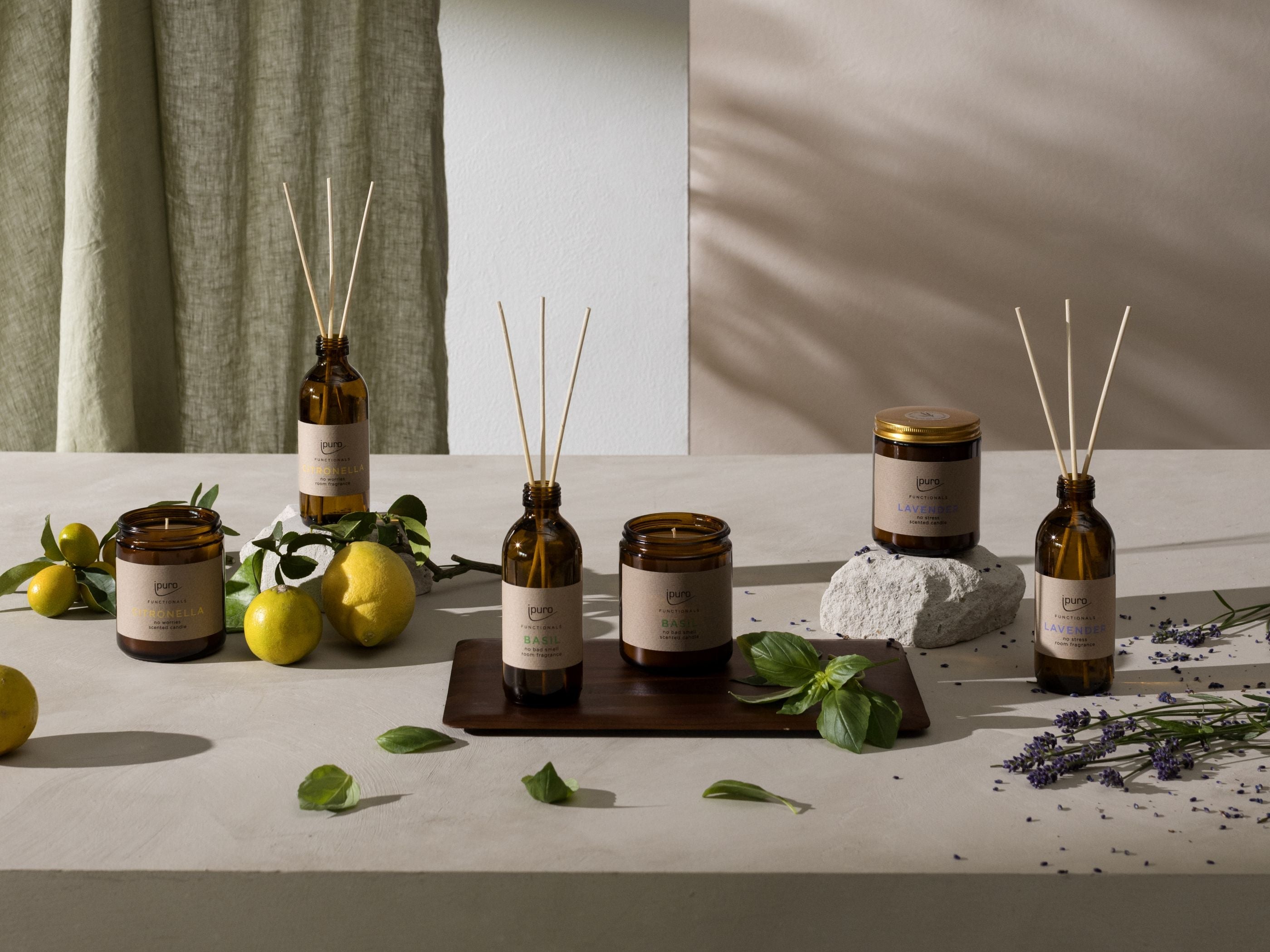 Bernsteinfarbene Gläser und Flaschen mit duftenden Produkten und Schilfrohrdiffusoren sind auf einer beigen Fläche angeordnet, umgeben von Zitronen, grünen Blättern, Lavendel und minimalistischem Dekor in natürlichem Licht.