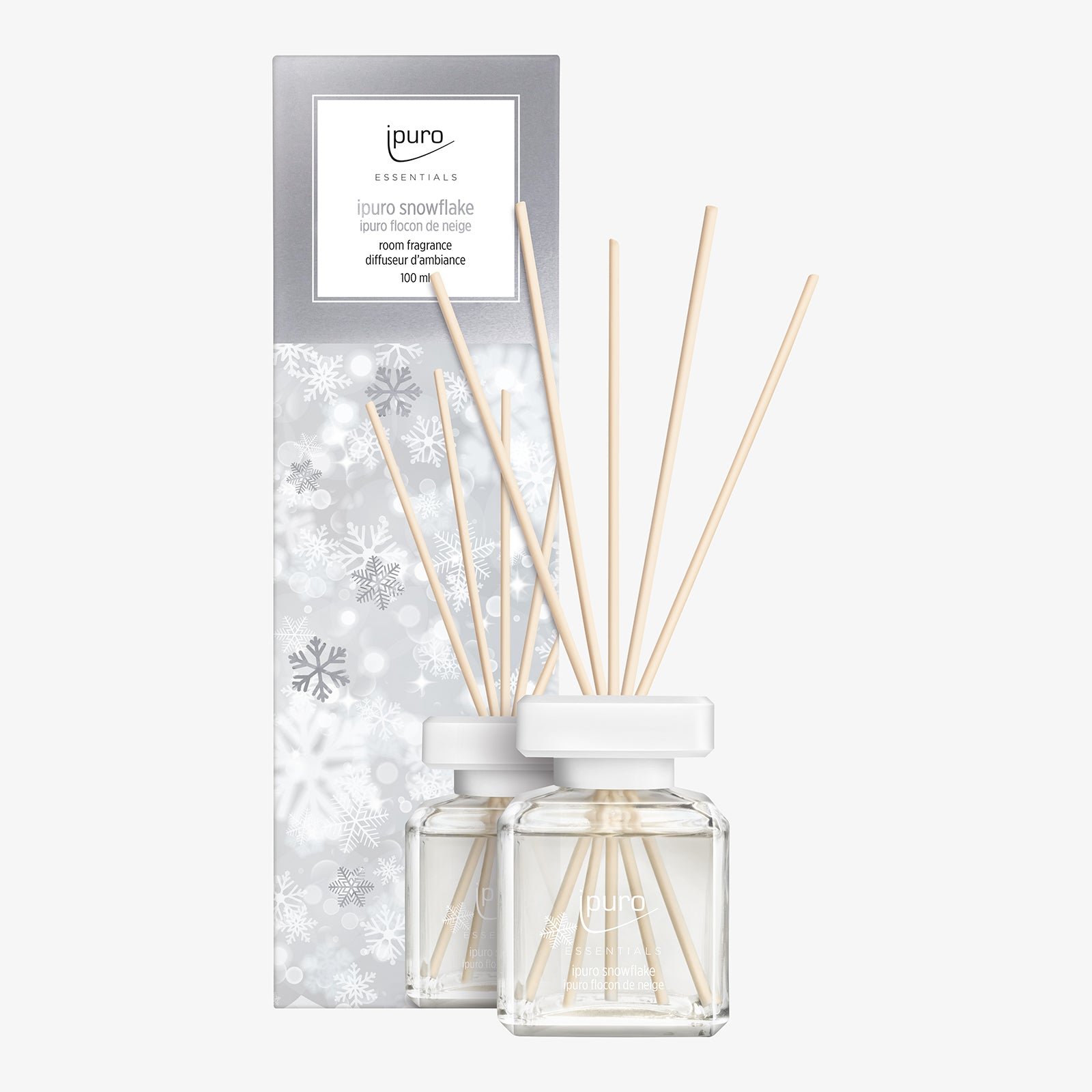 Der ipuro ESSENTIALS Raumduft Snowflake in einem klaren Glasflakon mit Holzschilfrohr wird neben seiner silber-weißen Verpackung mit Schneeflockenmuster gezeigt.