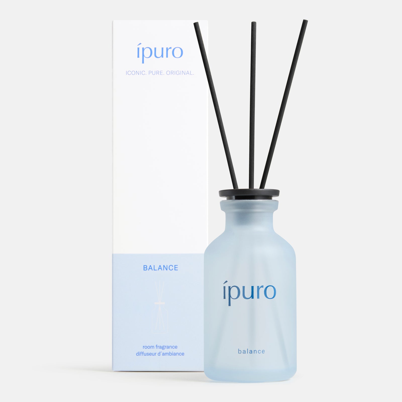 Ein Milchglasflakon mit der Aufschrift ipuro balance Raumduft by ipuro und drei schwarzen Diffusorstäben steht vor einer hohen weiß-hellblauen Schachtel mit passendem Branding und Text, die ein Gefühl von Ruhe und Leichtigkeit vermittelt.