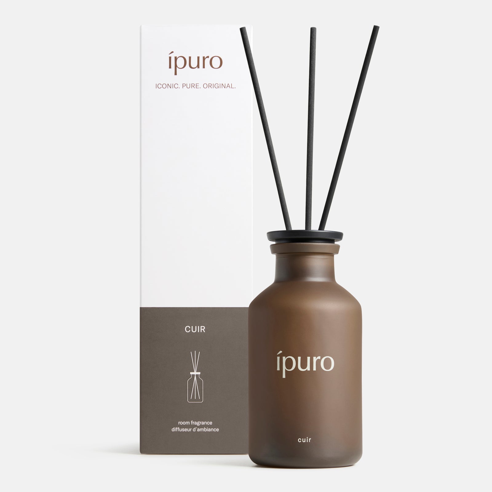 Ein brauner Glasflakon mit der Aufschrift ipuro und drei schwarzen Diffusorstäbchen steht neben einer weiß-braunen Schachtel mit den Aufschriften ipuro" und cuir". Beide stehen auf einem weißen Hintergrund und verströmen den warmen Duft von Raumduft ipuro cuir mit subtilen Zitrusnoten.