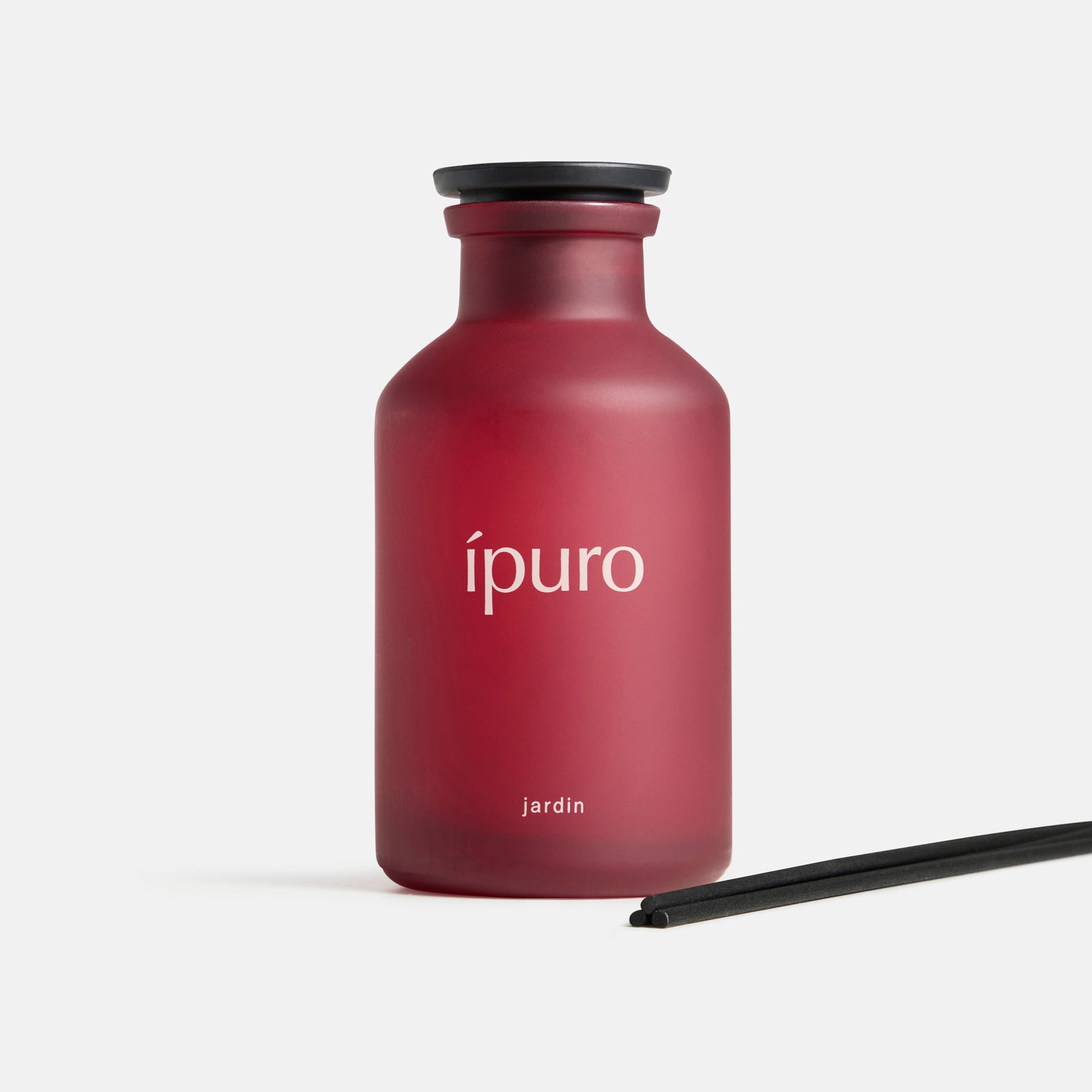 Ein mattroter Flakon mit der Aufschrift ipuro Raumduft CLASSIC jardin und einer schwarzen Kappe steht aufrecht, begleitet von zwei schwarzen Diffusorstäbchen - ein Hauch von exotischen Blüten aus einem verborgenen Garten - auf weißem Hintergrund.