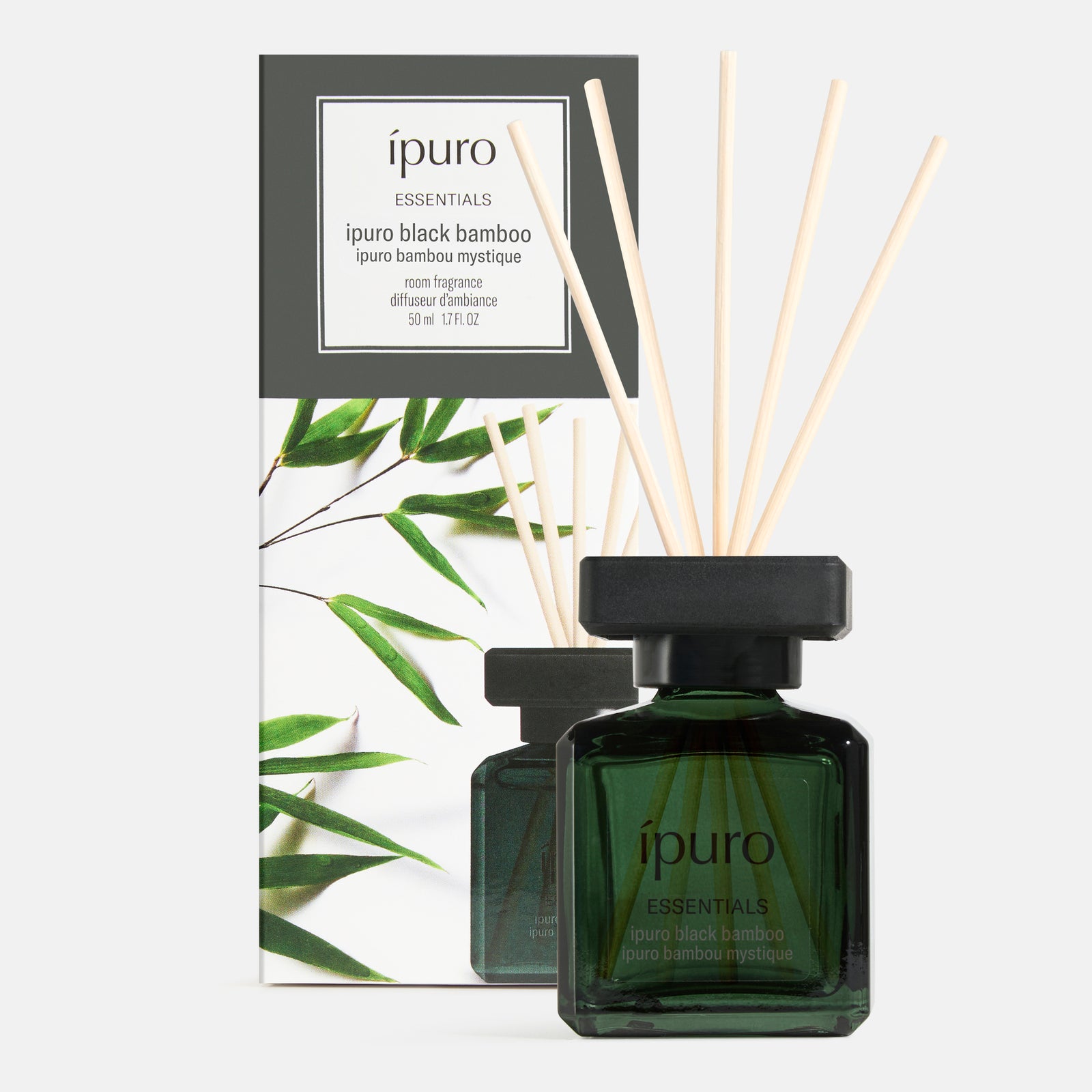 Ein grüner Glasflakon von Raumduft ipuro black bamboo by ipuro mit hölzernen Schilfrohrstäben steht vor seiner Schachtel mit Bambusblattmotiven und Branding, die grüne Frische und eine holzige Nuance vermitteln.