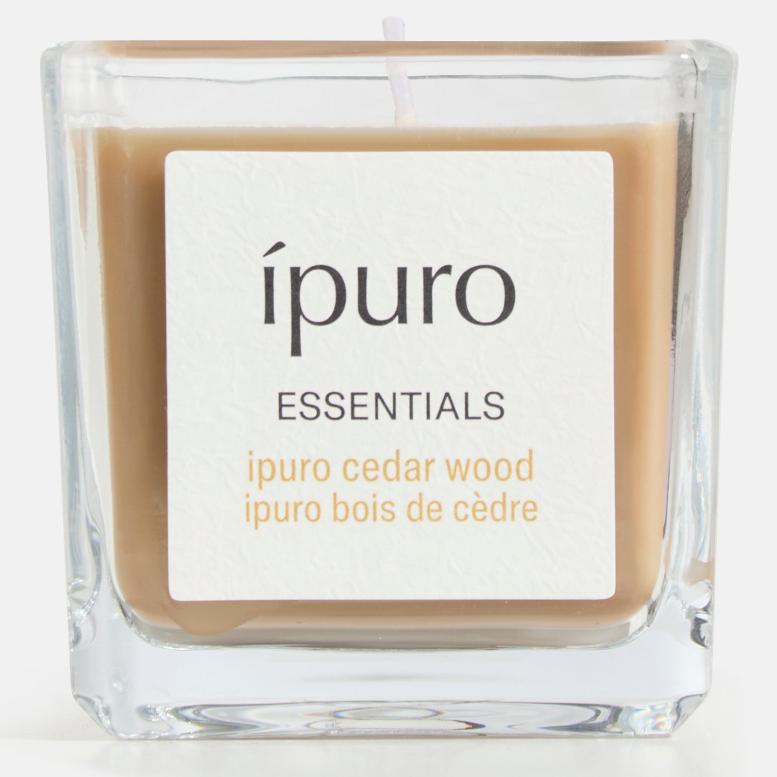 Die quadratische Glas-Duftkerze ipuro cedar wood von ipuro mit hellbraunem Wachs und einem warmen, holzigen Duft schafft eine gemütliche, einladende Atmosphäre. Die Duftangaben auf dem Etikett sind auf Englisch und Französisch.