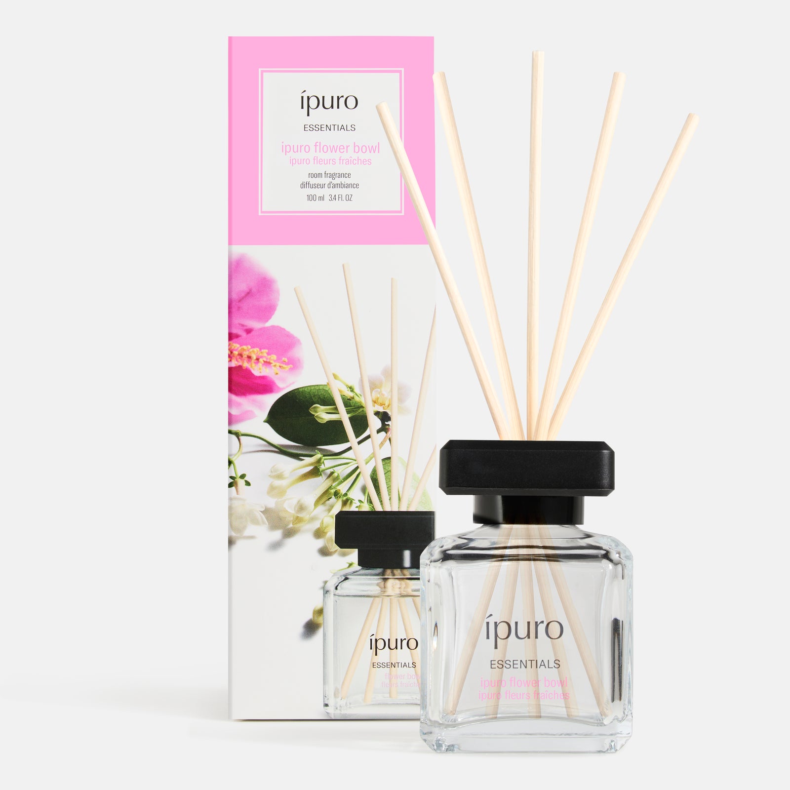 Ein Glasflakon von ipuro Raumduft lovely flowers mit fünf Holzstäbchen und floralen Noten steht vor seiner dekorativen Verpackungsschachtel.