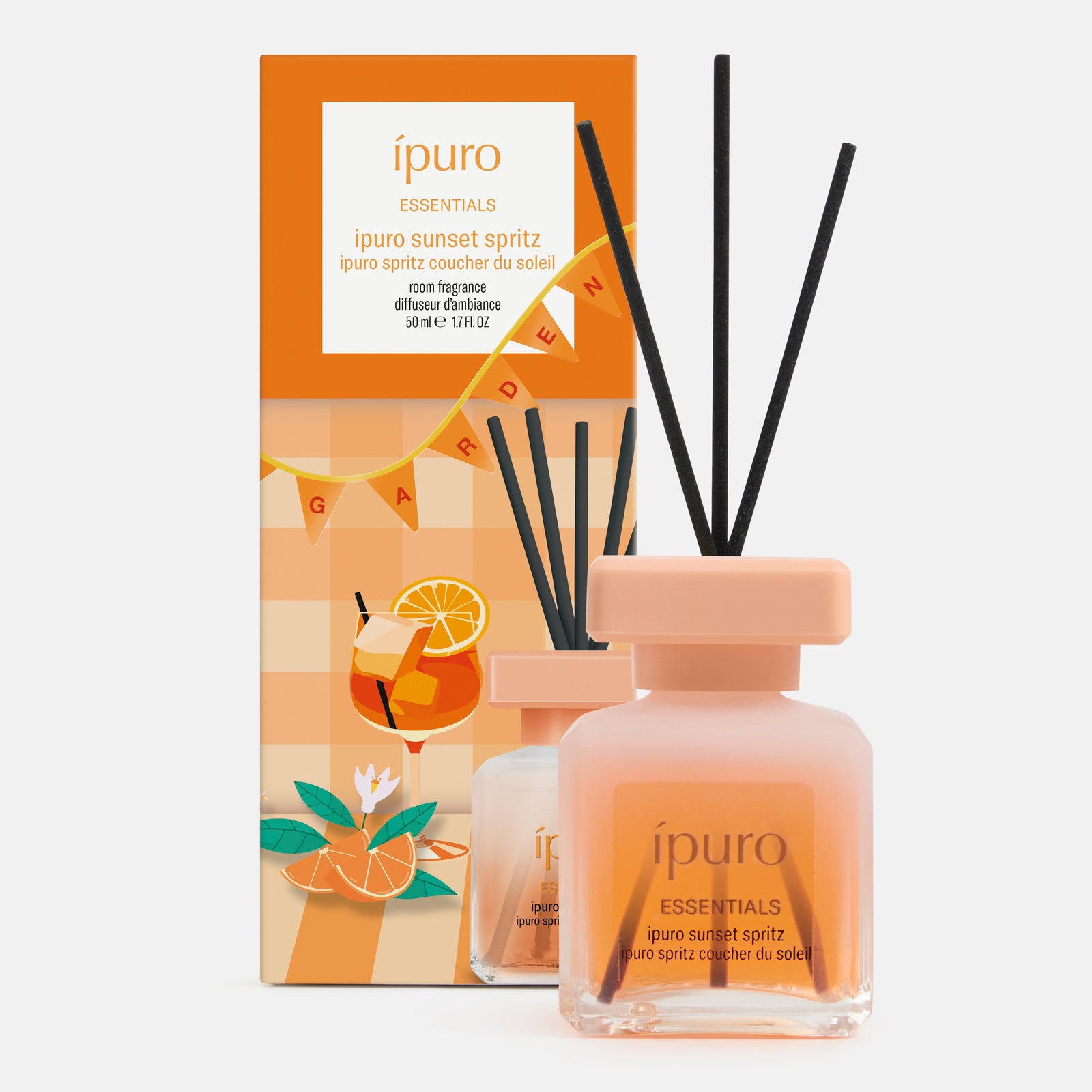 Abgebildet ist ein verpackter ESSENTIALS ipuro sunset spritz Rohrdiffusor von ipuro. Die pfirsich- und orangefarbene Verpackung ist mit Zitrusfrüchten und Blumen verziert, die den frischen Duft im Inneren andeuten. Die vordere Flasche enthält orangefarbene Flüssigkeit mit schwarzem Schilfrohr.