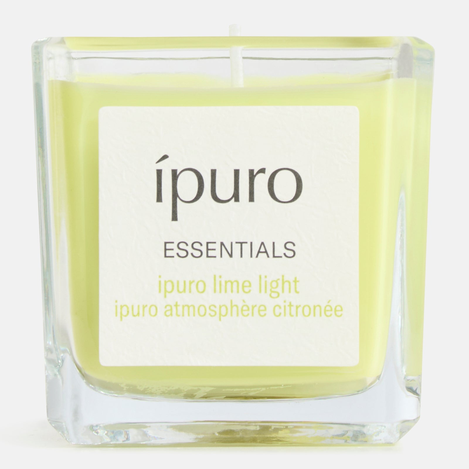 In einem quadratischen Glashalter befindet sich eine hellgelbe ipuro Duftkerze Limette mit der Aufschrift ipuro ESSENTIALS" und ipuro atmosphère citronée". Sie duftet nach Zitronengras und verspricht Frische auf weißem Grund.