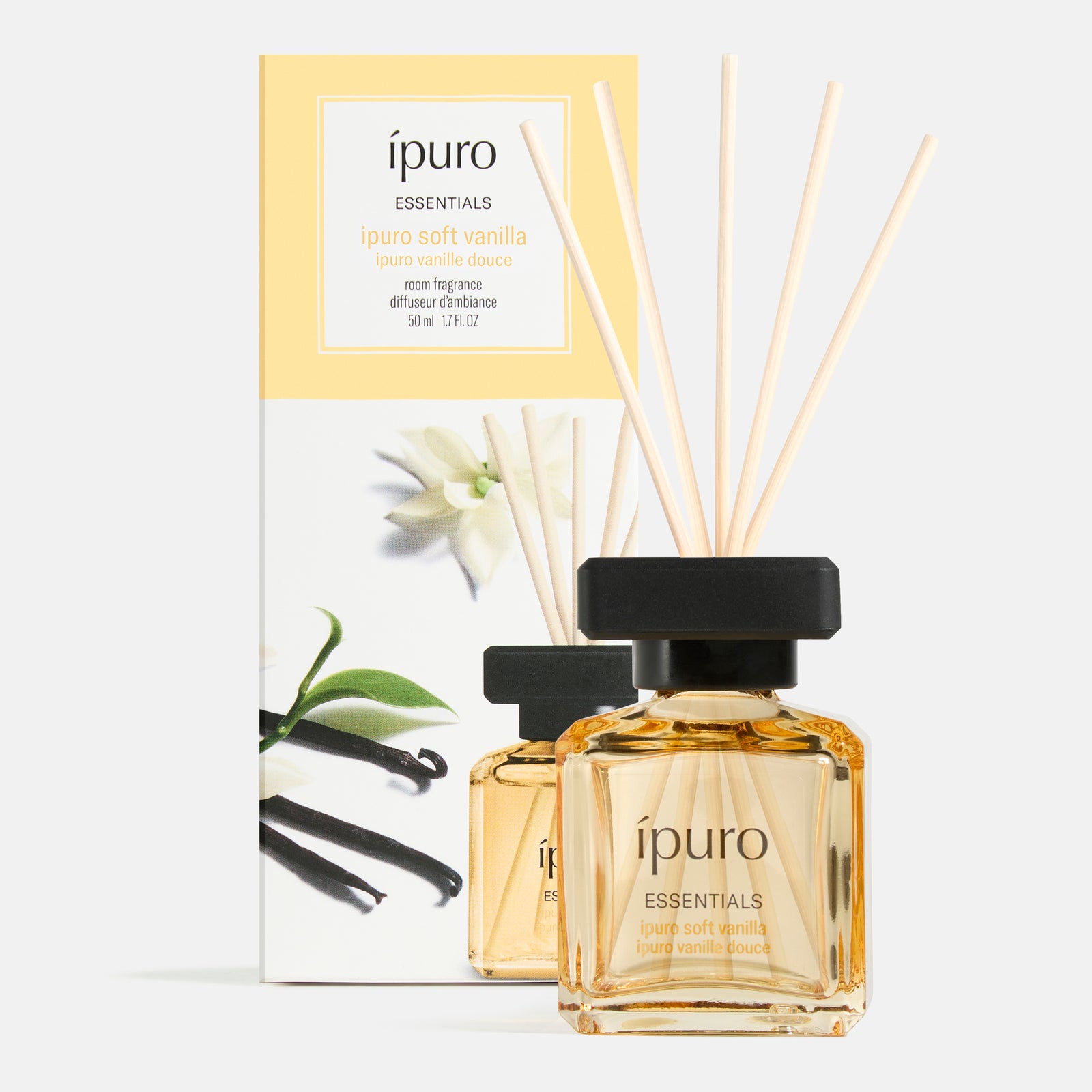 Ein Flakon von ipuro Raumduft soft vanilla diffuser mit Holzstäbchen sitzt vor seiner mit Vanilleblüten und -schoten verzierten Box. Die leicht bernsteinfarbene Flüssigkeit von ipuro bietet warme Vanillenoten und einen Hauch von Sandelholz.