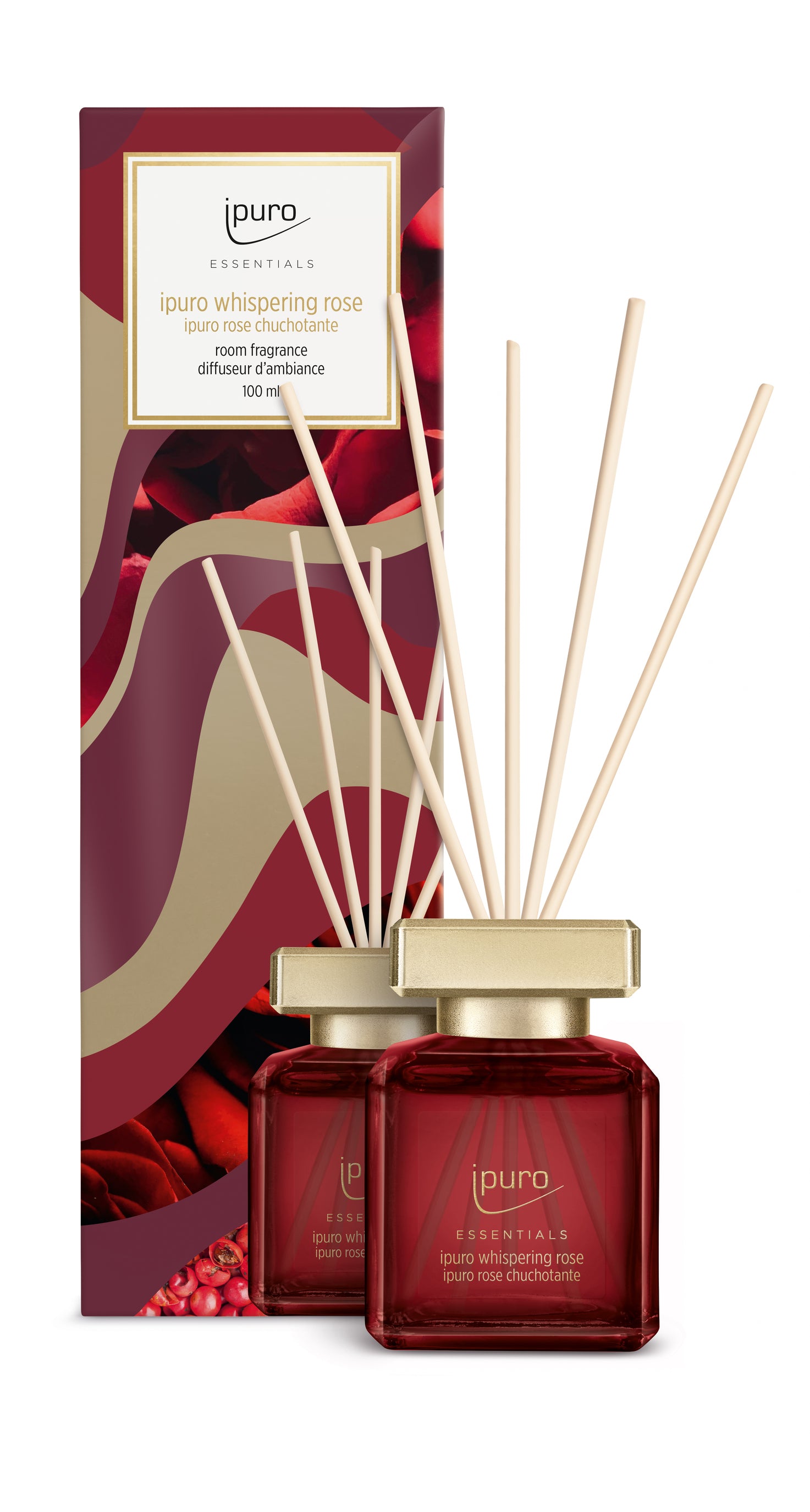 Der ESSENTIALS ipuro whispering rose Raumduft von ipuro präsentiert sich in einem roten Glasflakon mit Holzschilfrohr, der fruchtige Noten und holzige Aromen bietet, vor seiner dekorativen Schachtel mit Rosenmuster und Goldakzenten.