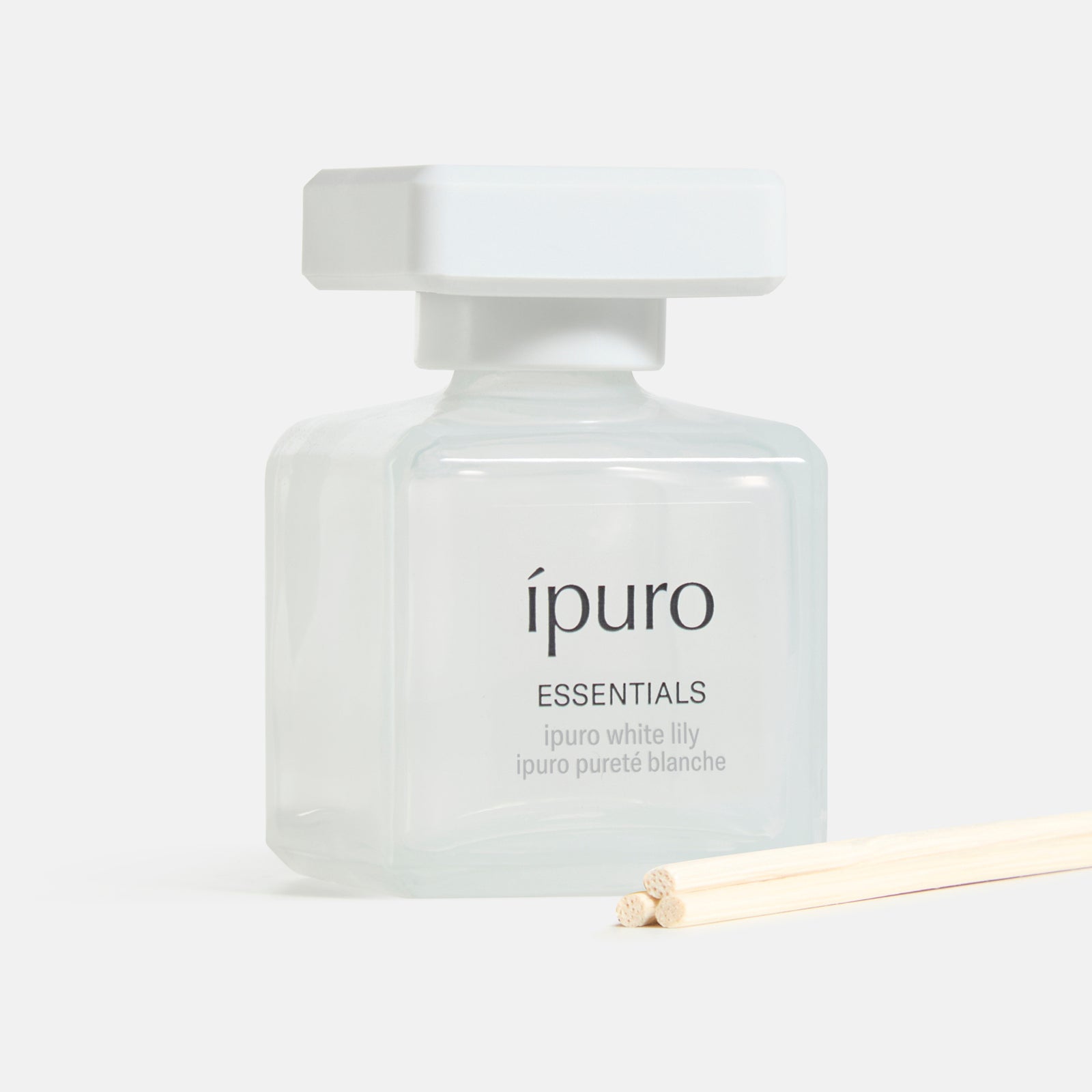Der ipuro Raumduft white lily, eine quadratische Glasflasche mit weißem Verschluss und dünnen Holzstäbchen, bietet ein blumiges Dufterlebnis und einen zarten Duft von weißer Blüte - alles von ipuro.